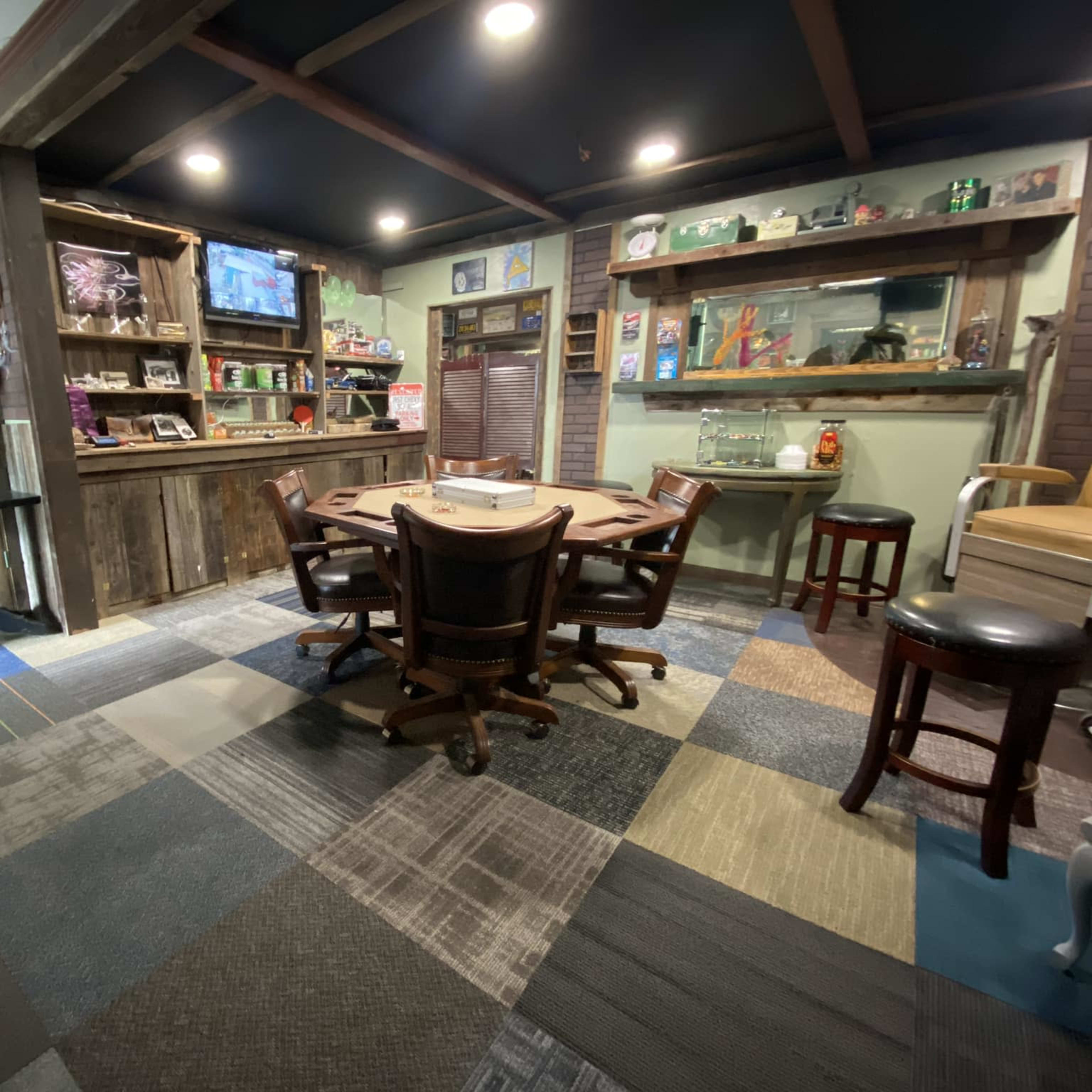 A game room with a circular wooden table surrounded by chairs, a television mounted on the wall, and shelves filled with various items.