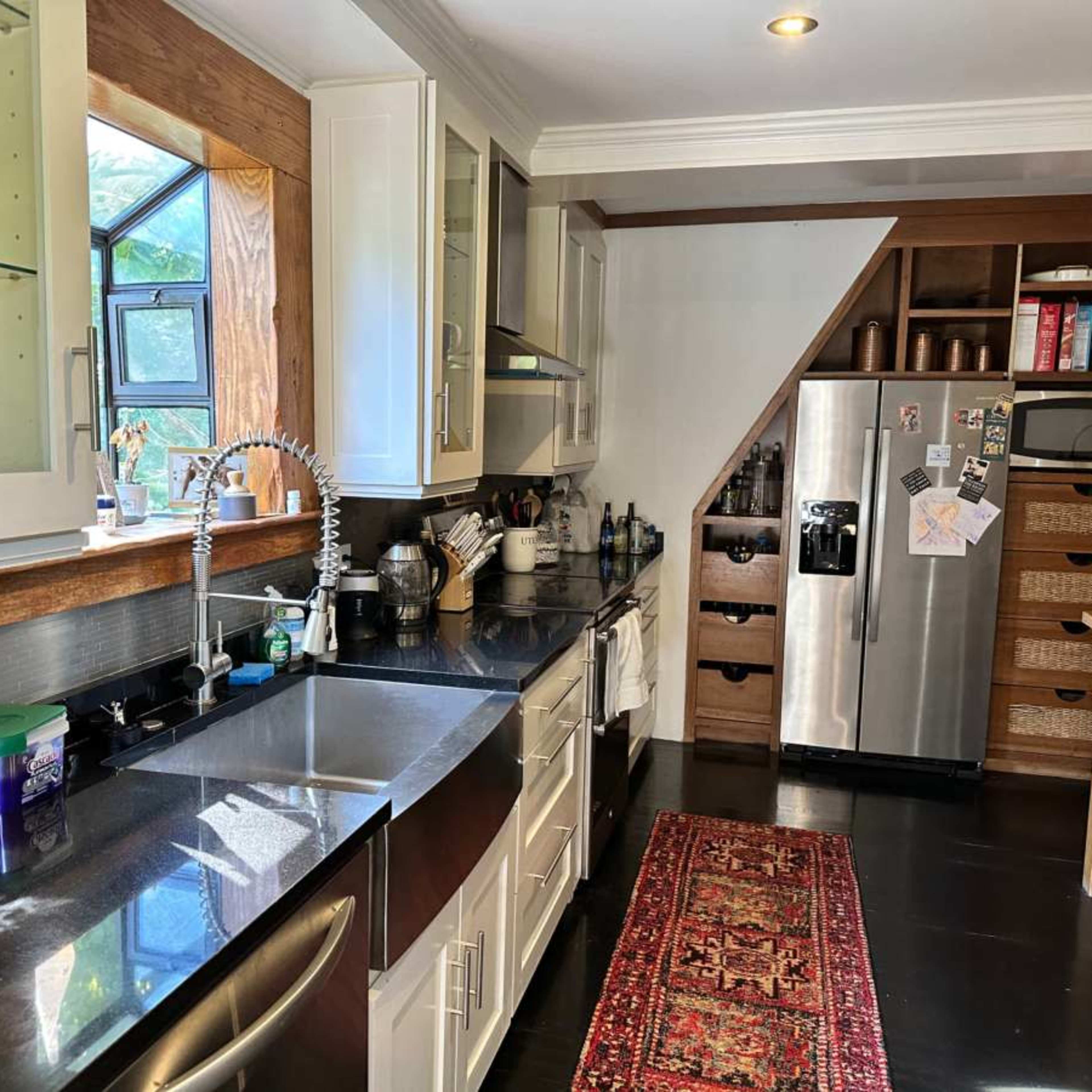 A modern kitchen with a stainless steel refrigerator, dark countertops, and light-colored cabinetry, featuring a small dining area and various kitchen appliances.
