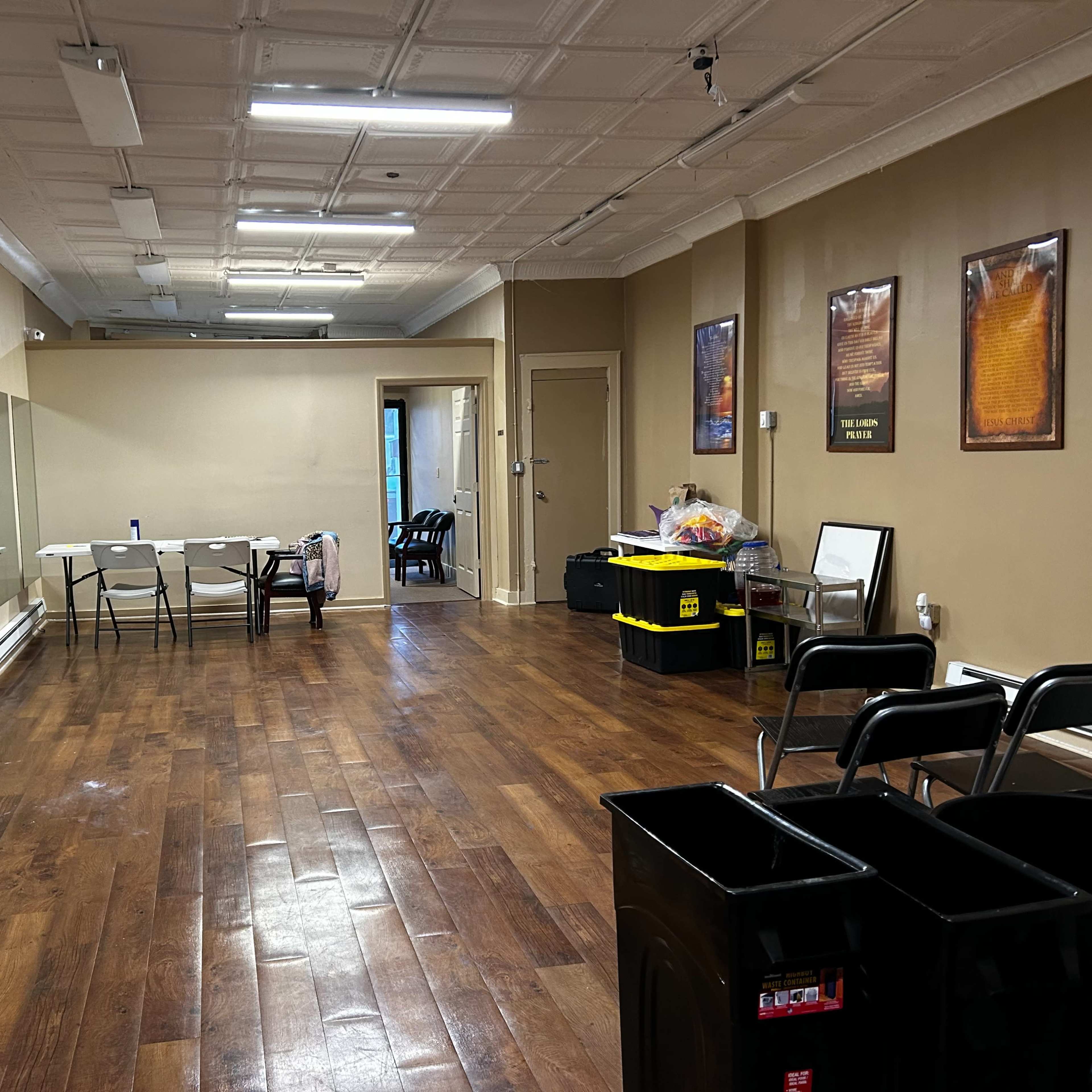 An empty room with wooden flooring, a large mirror on one wall, and several folding chairs arranged along the side.