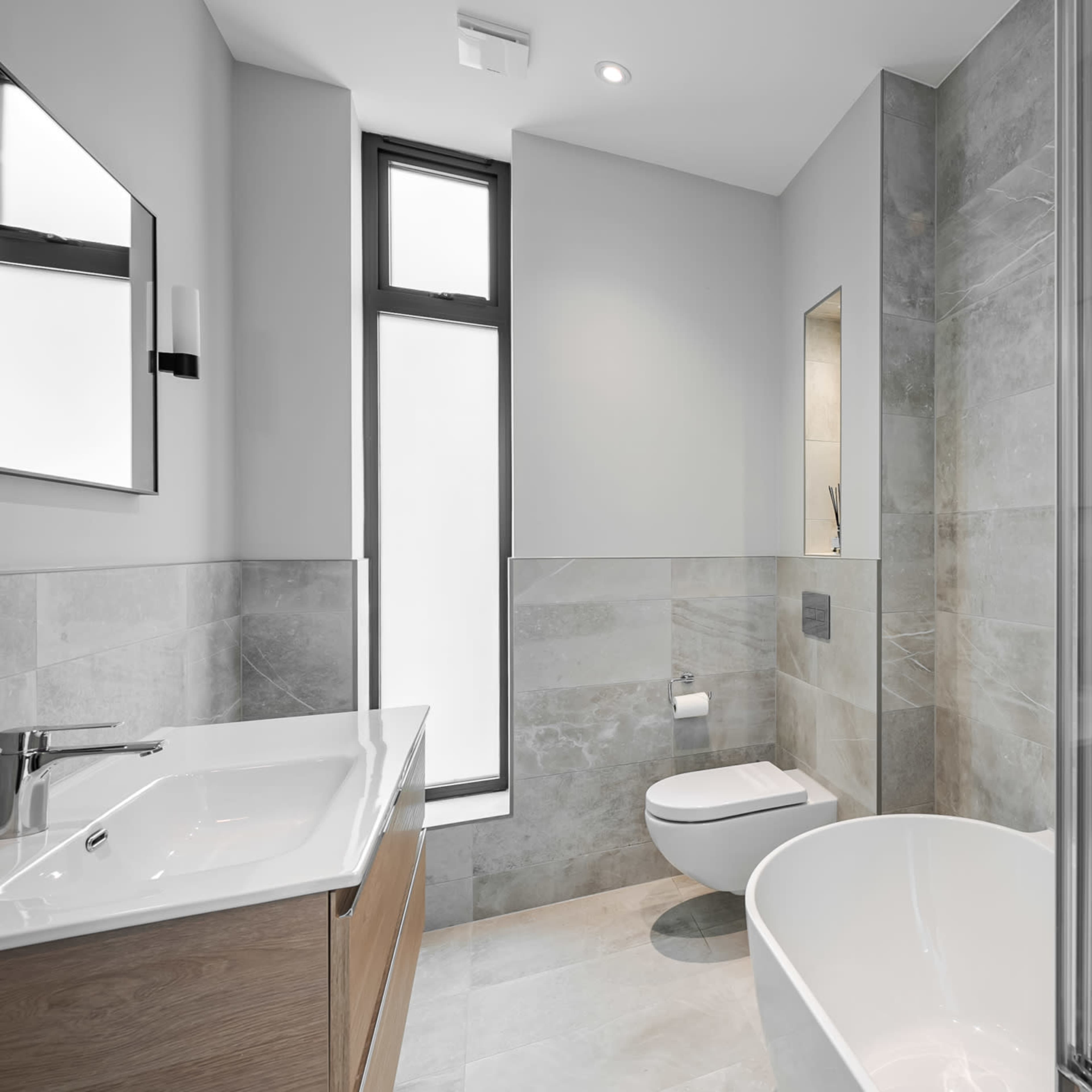 A modern bathroom featuring a freestanding tub, a wall-mounted toilet, and a large window for natural light.