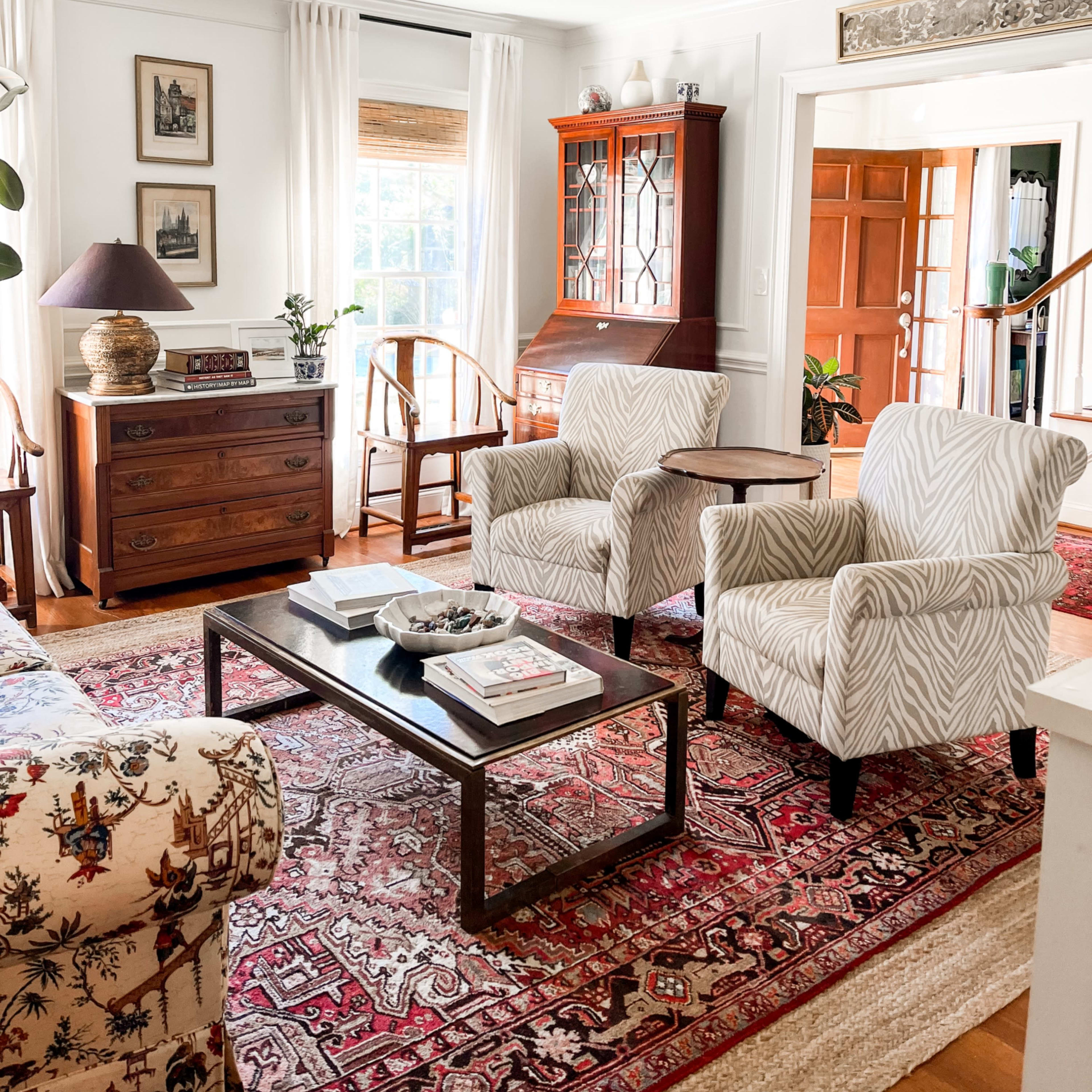 The living room features a patterned rug, two upholstered chairs, a wooden coffee table, and a cabinet against a bright window.