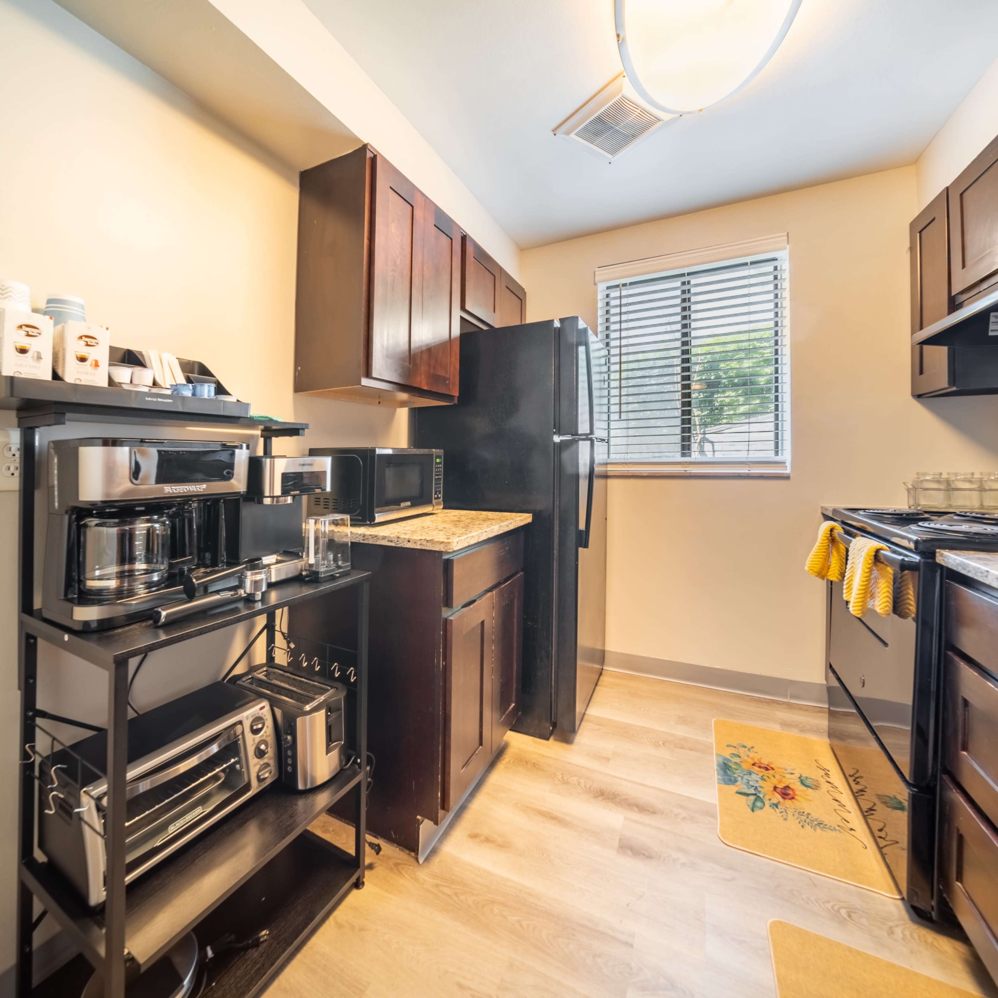 A compact kitchen featuring dark wooden cabinets, a black refrigerator, and an oven with a nearby countertop space.