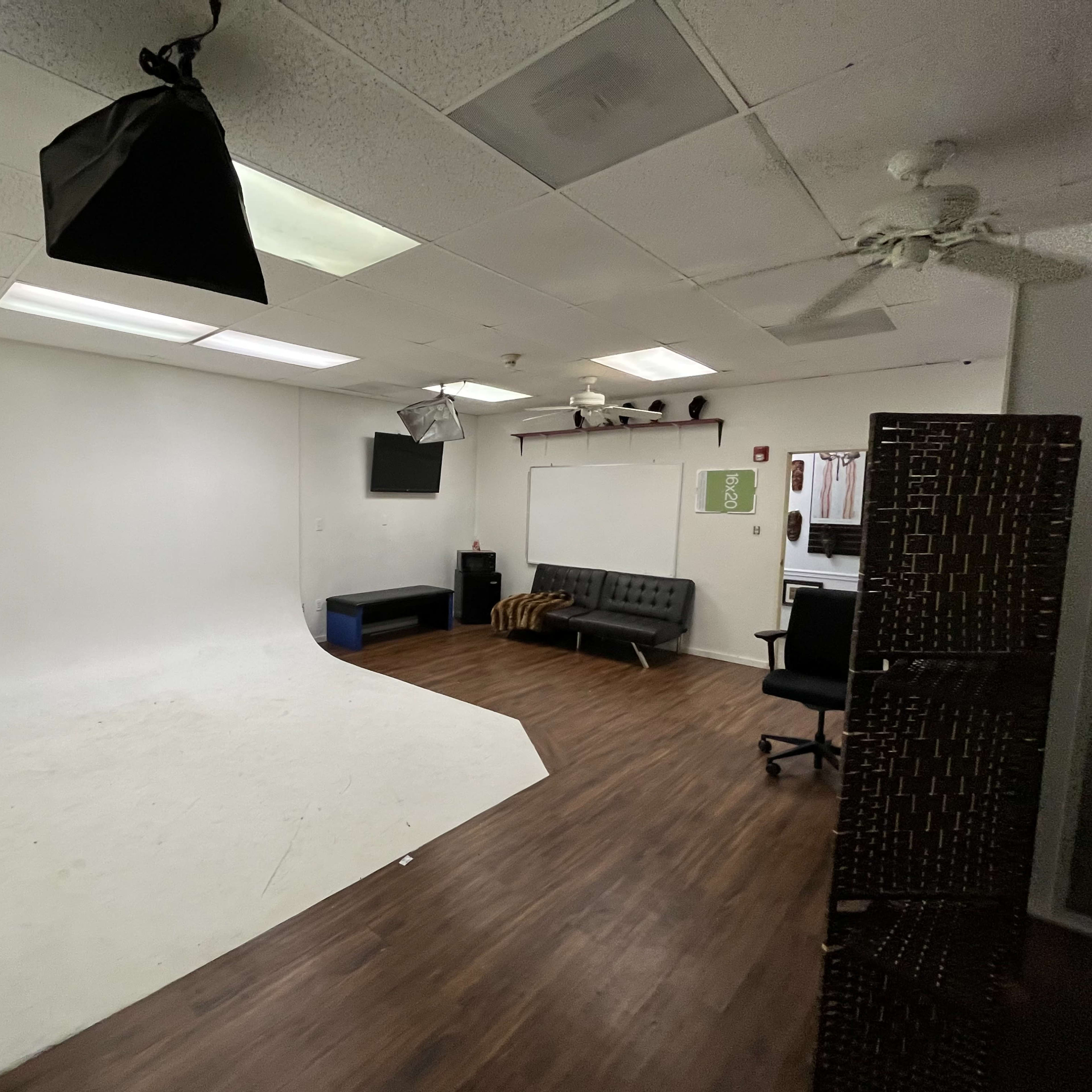 A spacious, empty studio with a curved white backdrop, hardwood floor, and various lighting equipment mounted on the ceiling.