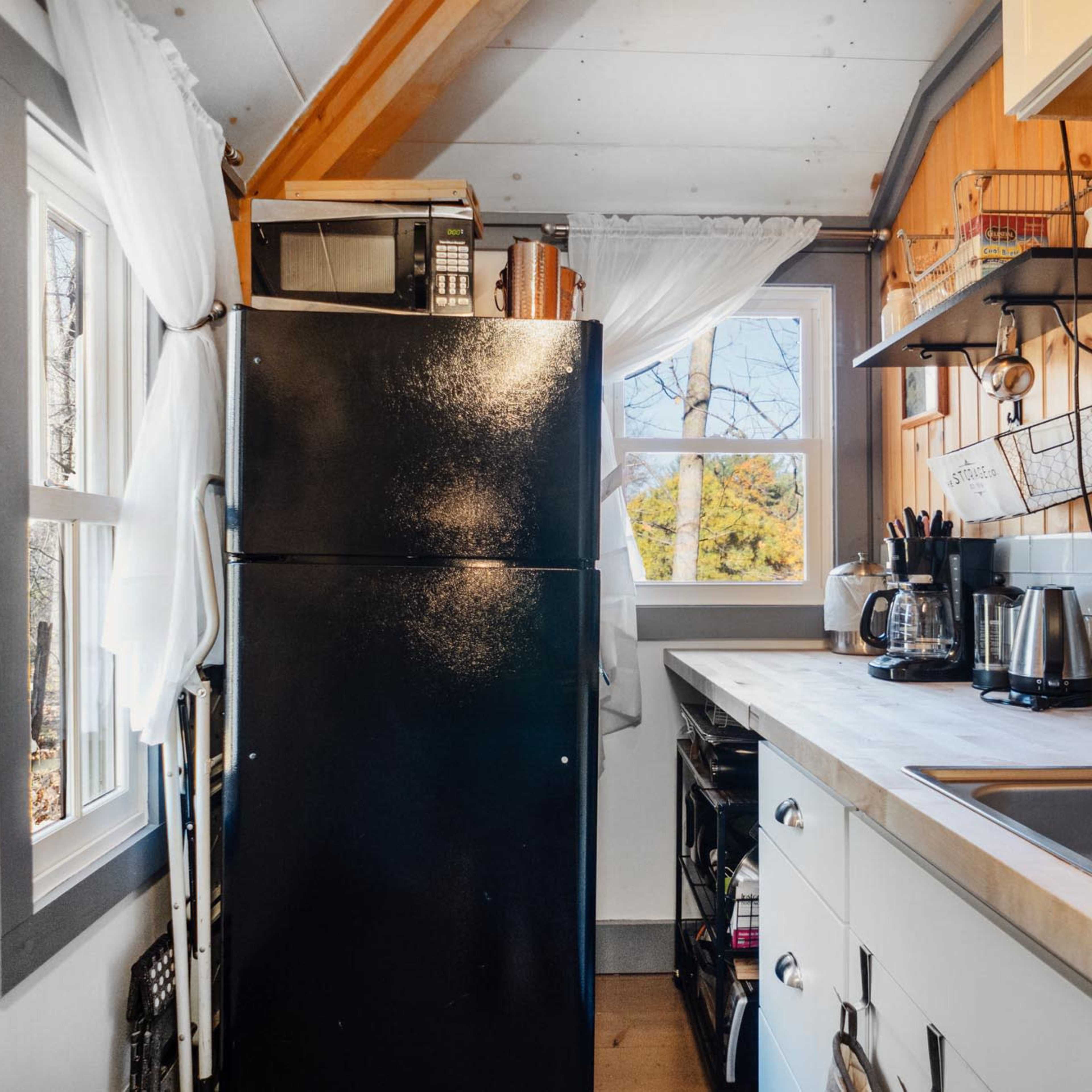 A compact kitchen features a black refrigerator, a sink, and shelves with various kitchen utensils.