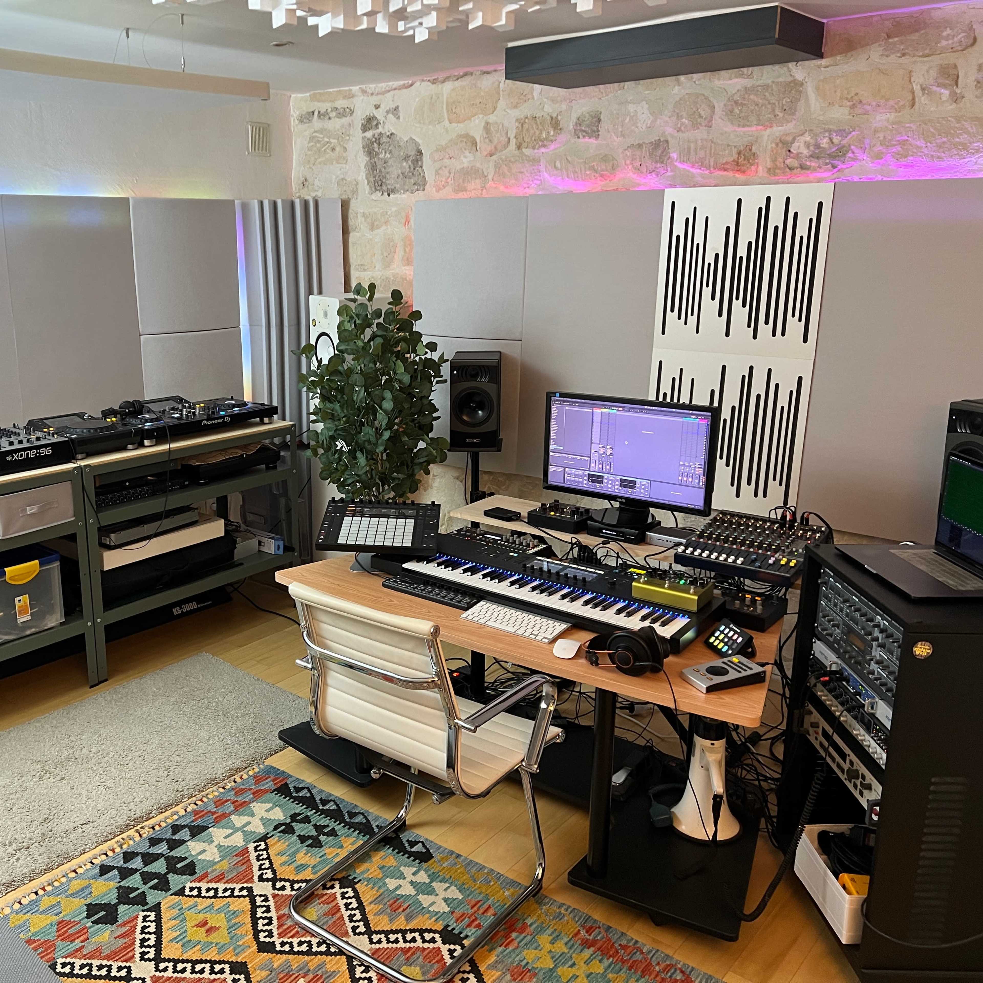 A music production studio featuring turntables, a keyboard, various audio equipment, and a desk with a computer setup.
