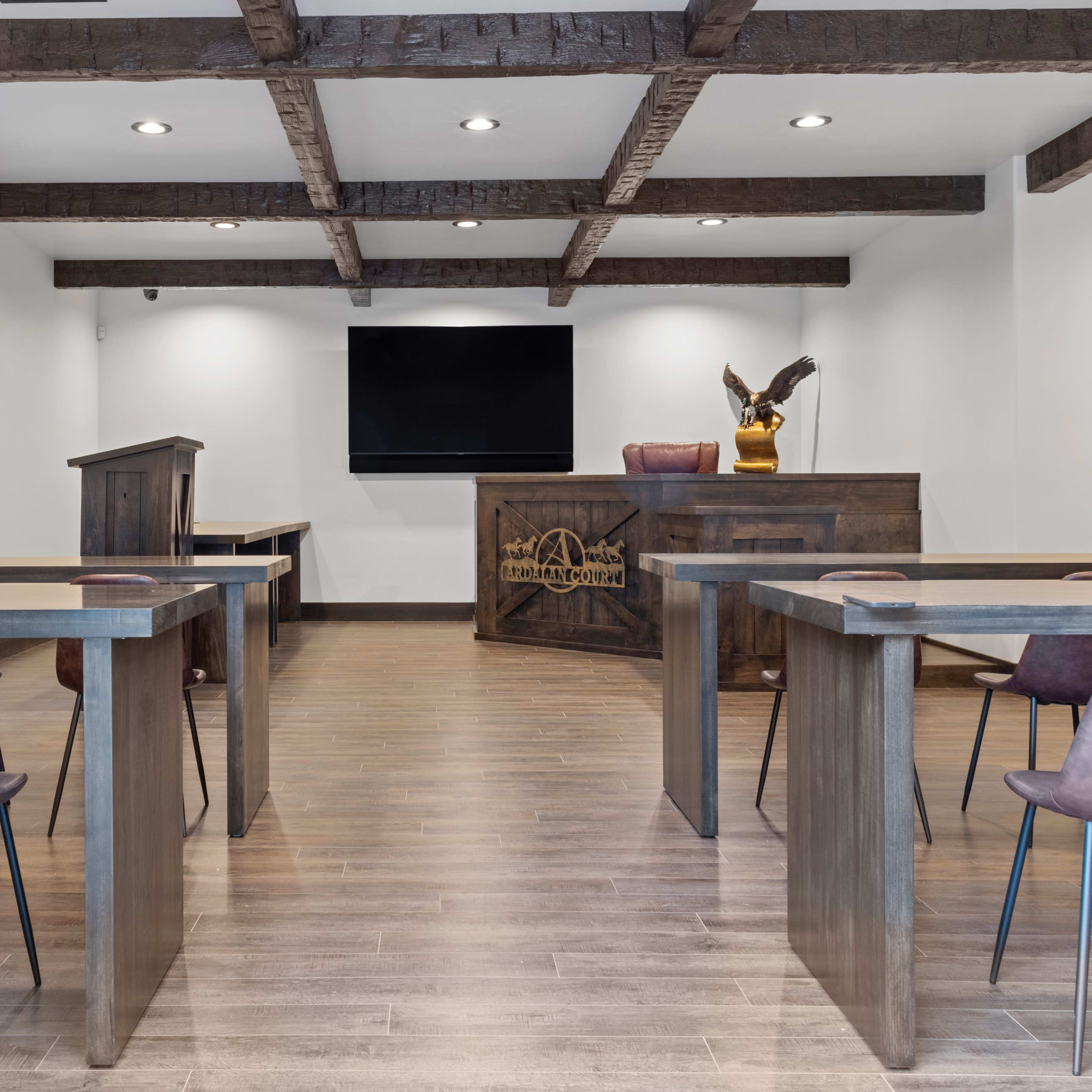 A modern conference room featuring wooden beams, a reception desk with a monitor, and several tables with chairs arranged for a meeting.