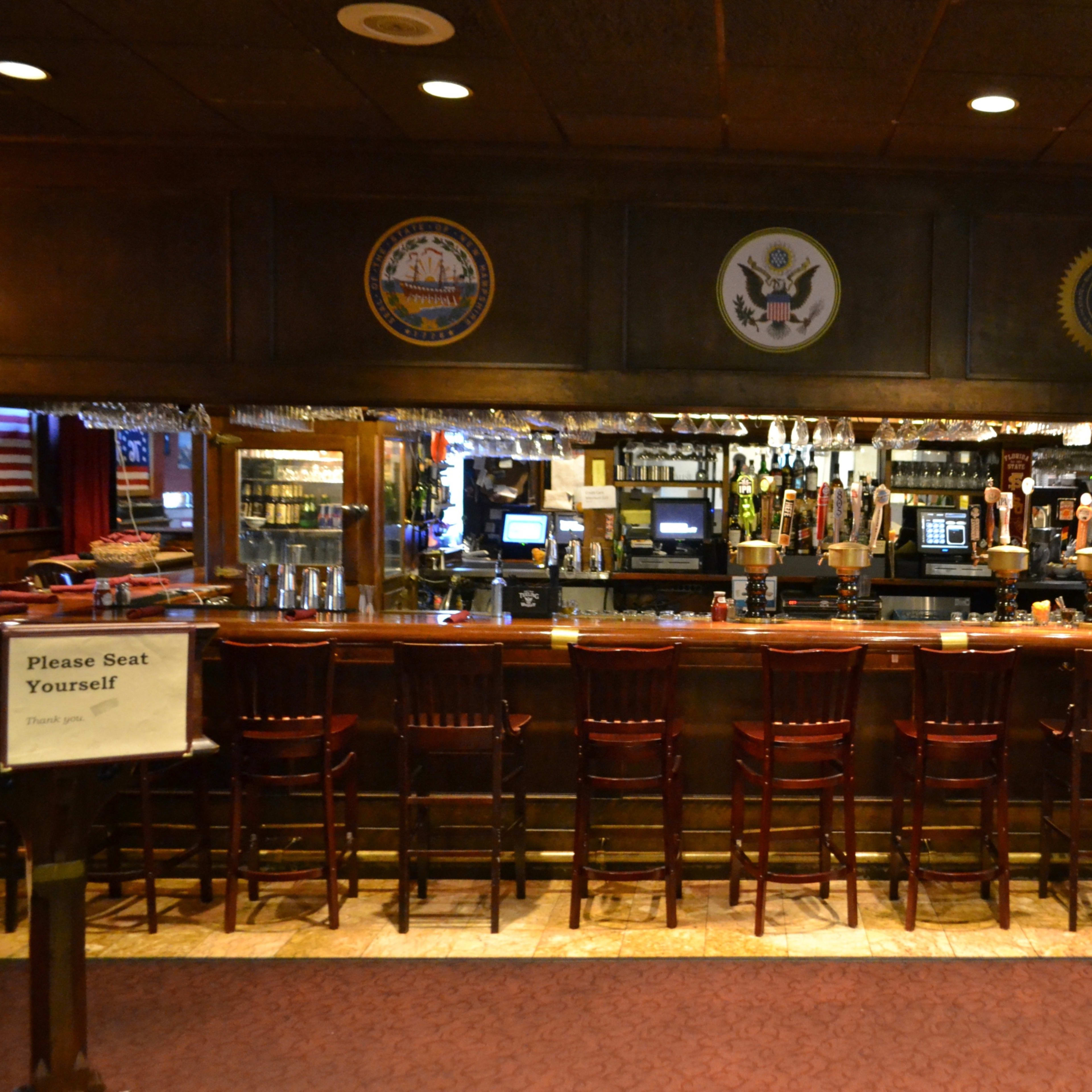 A wooden bar with empty stools and various emblems displayed on the wall behind it.