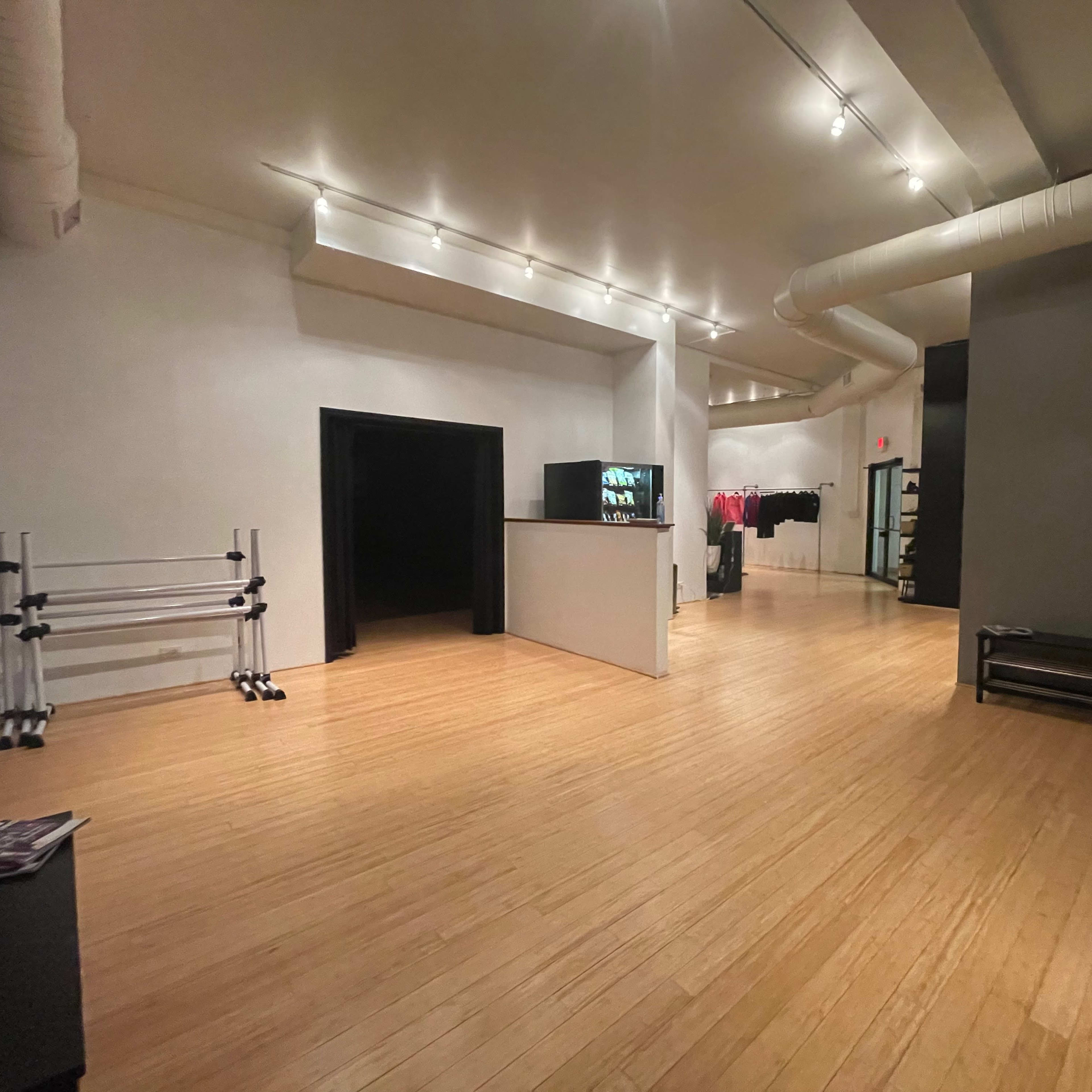 A spacious, empty room with wooden flooring and minimalist decor, featuring a reception area and clothing racks along the walls.