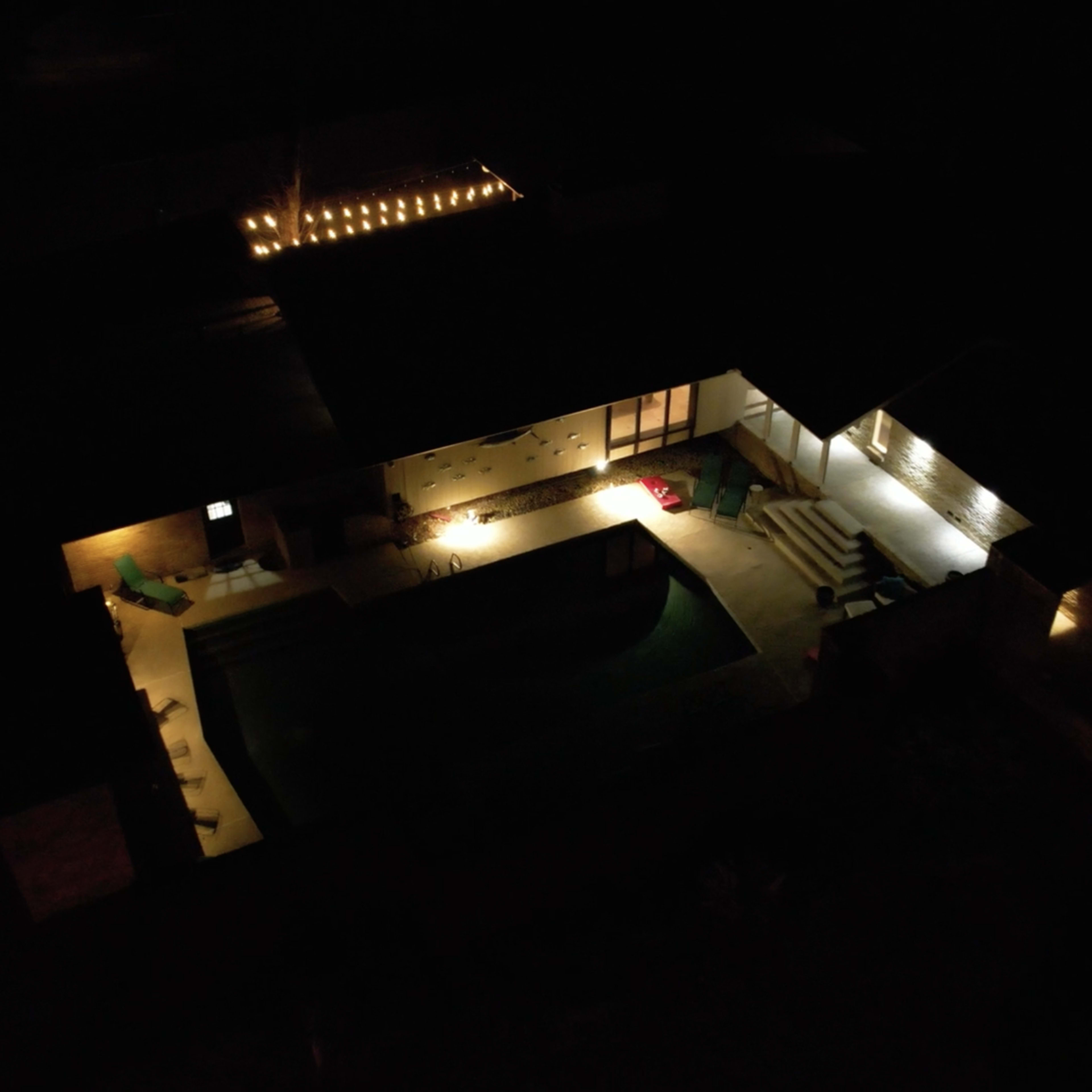 Aerial view of a house at night, illuminated by exterior lights around a swimming pool.