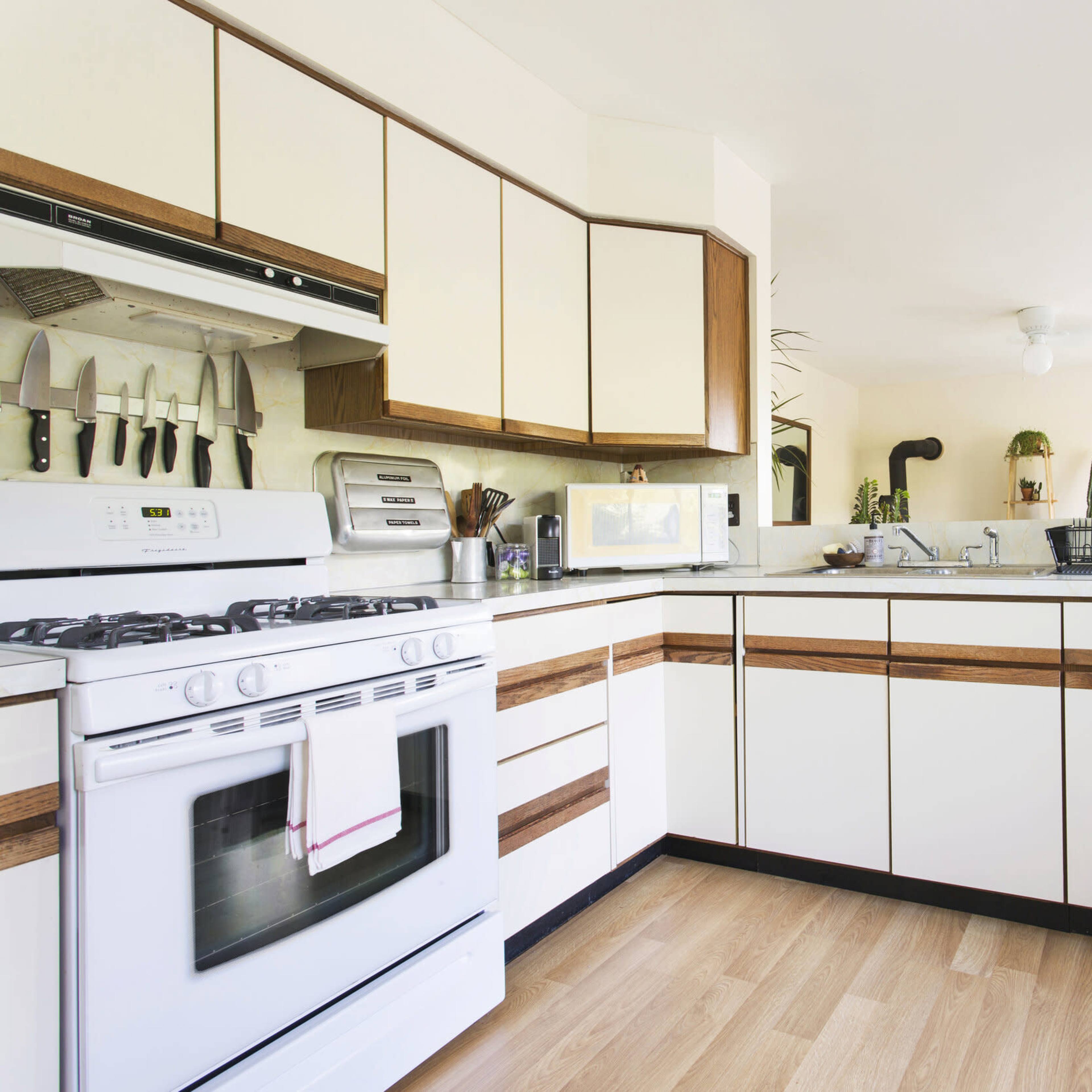 A modern kitchen features white cabinetry with wood accents, a gas stove, and large windows adorned with plants.