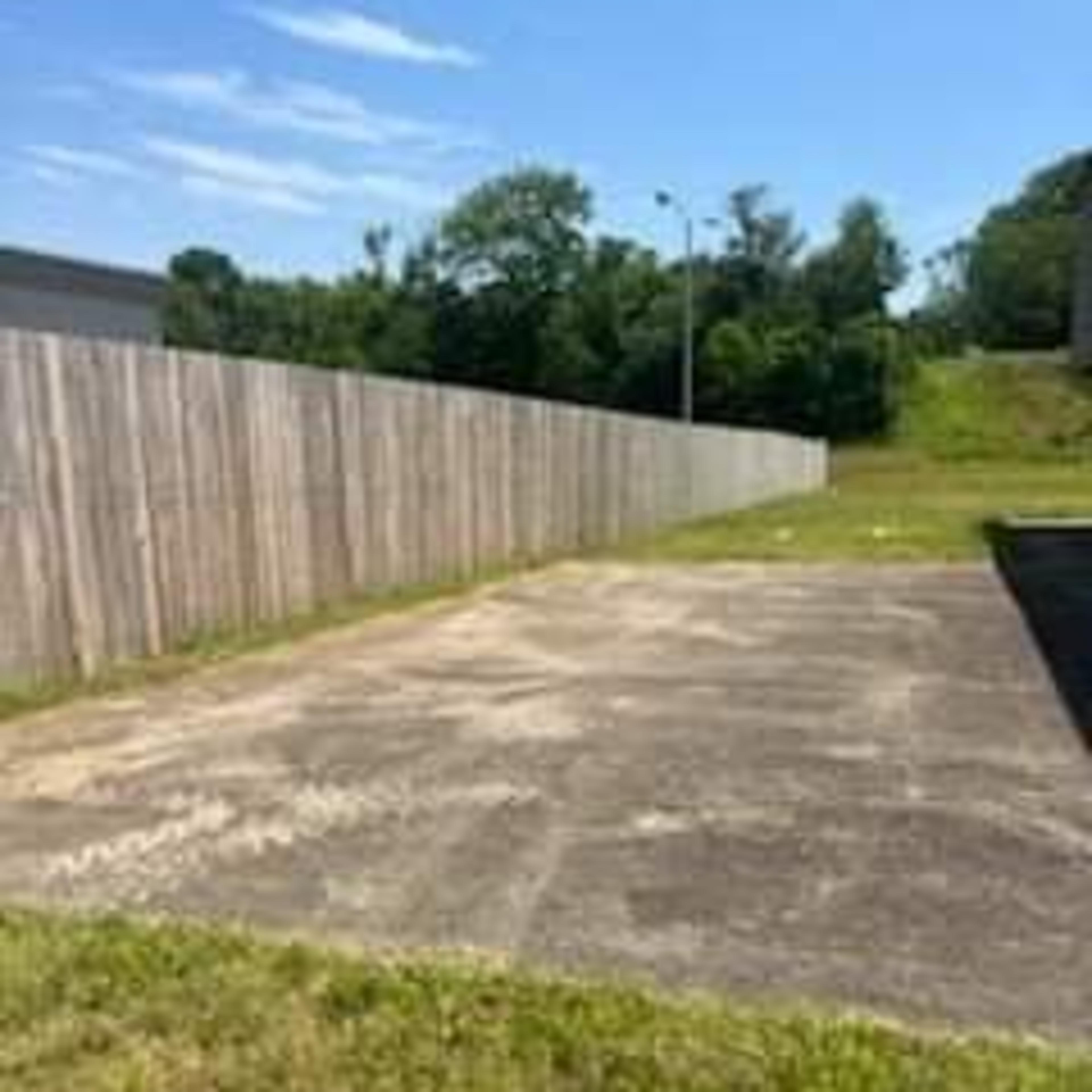 An empty, concrete area surrounded by a wooden fence and grass under a clear blue sky.