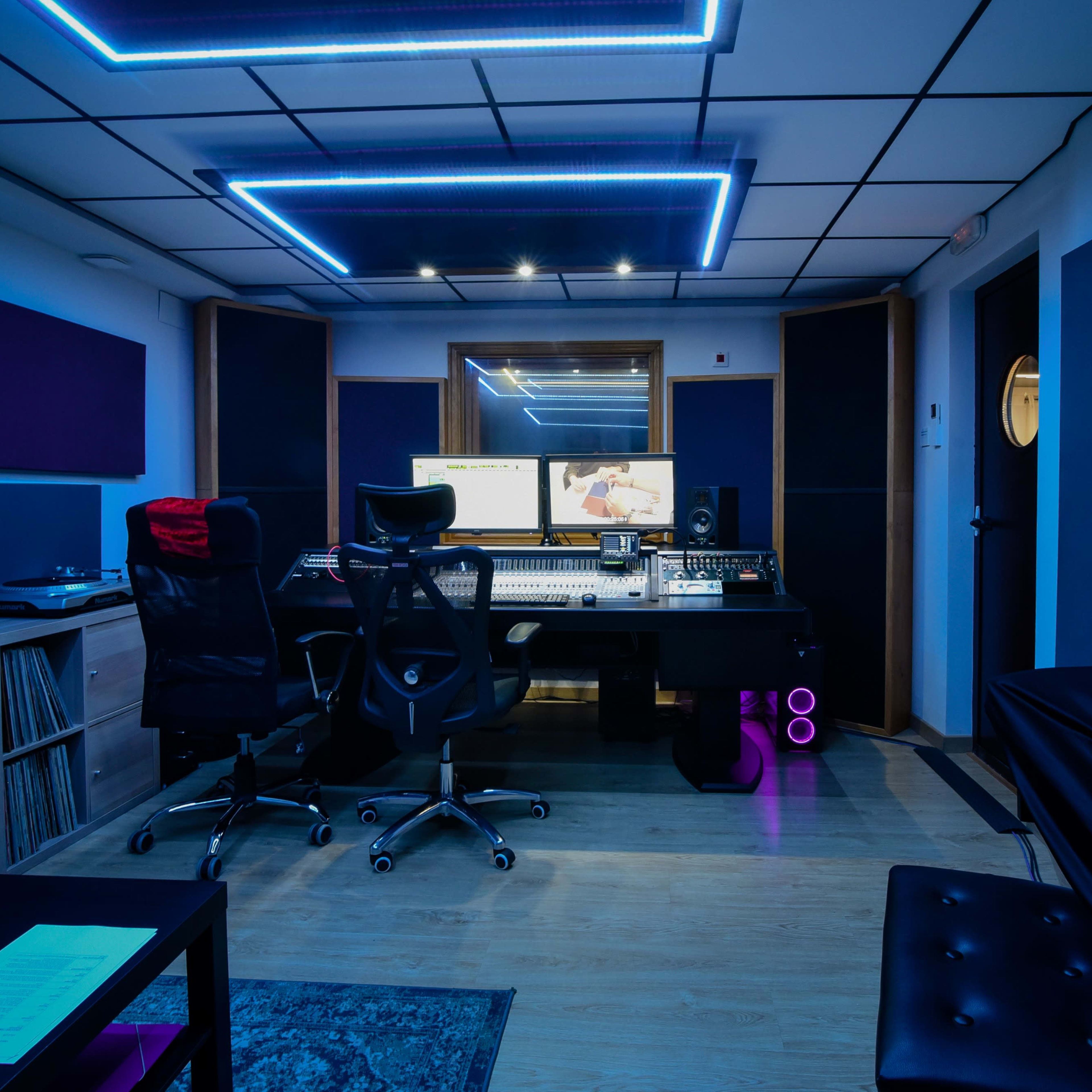 A modern recording studio with sound equipment, a large mixing console, and ambient blue lighting.