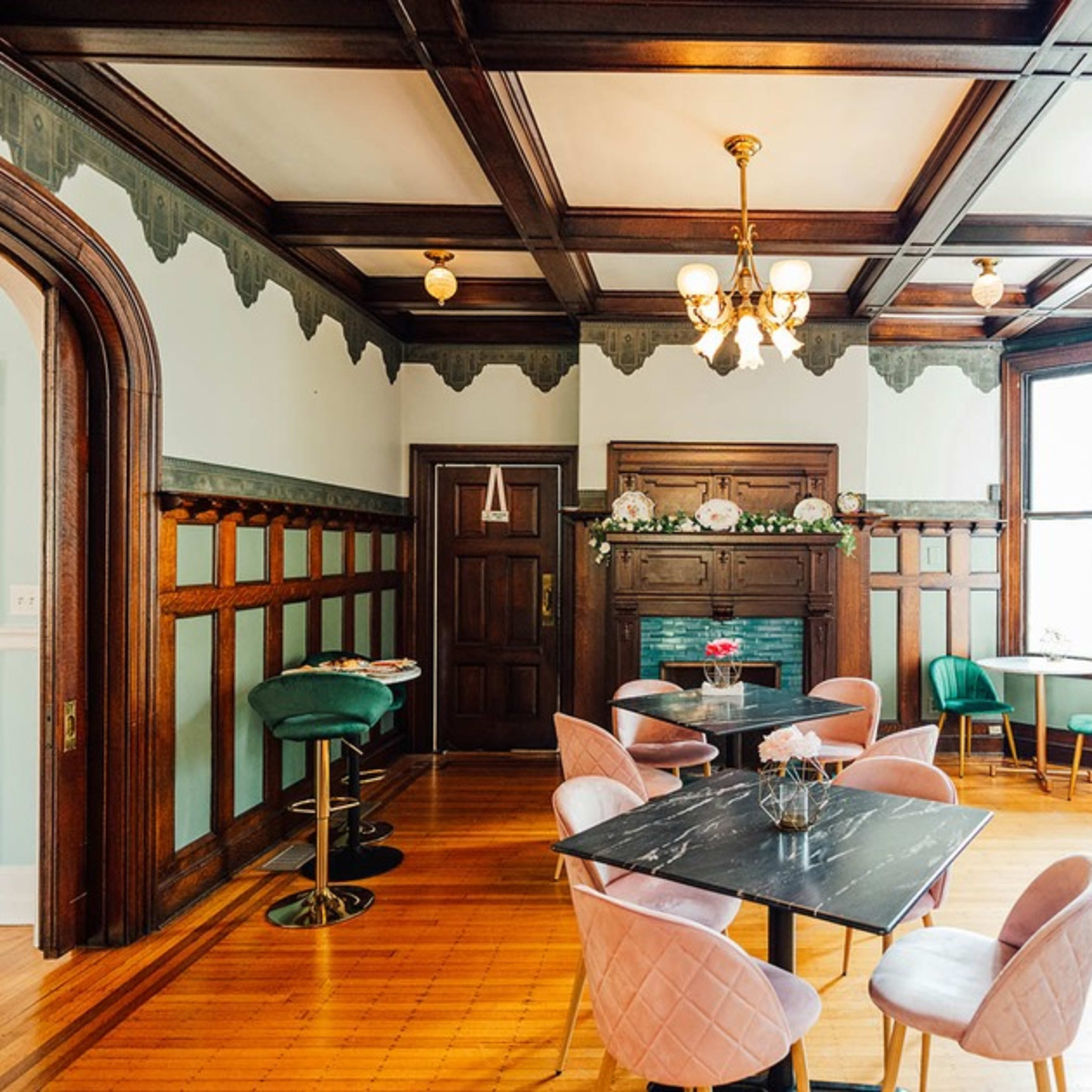 An elegantly furnished room with dark wooden paneling, a fireplace, and various seating arrangements, including pink and green chairs around a dark marble table.