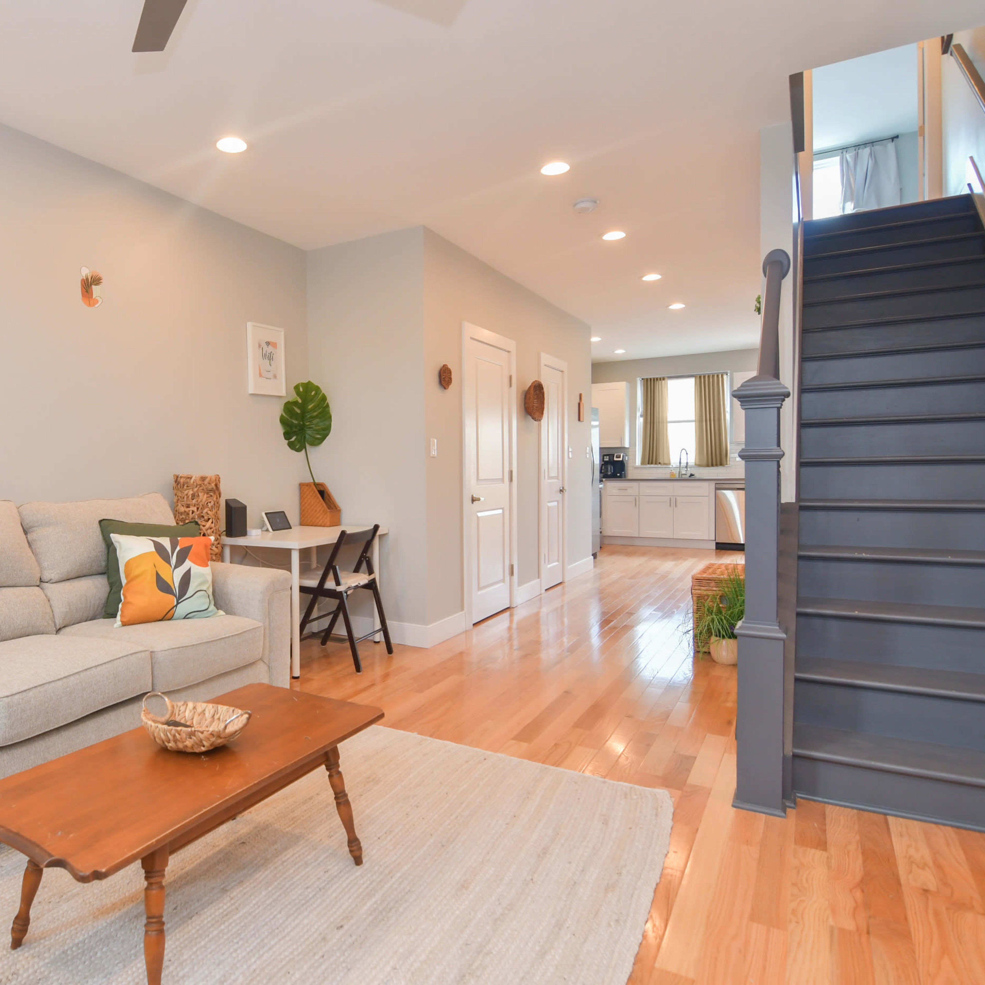 A stylish living room with a light gray sofa and a wooden coffee table, leading to a staircase and an open kitchen area in the background.