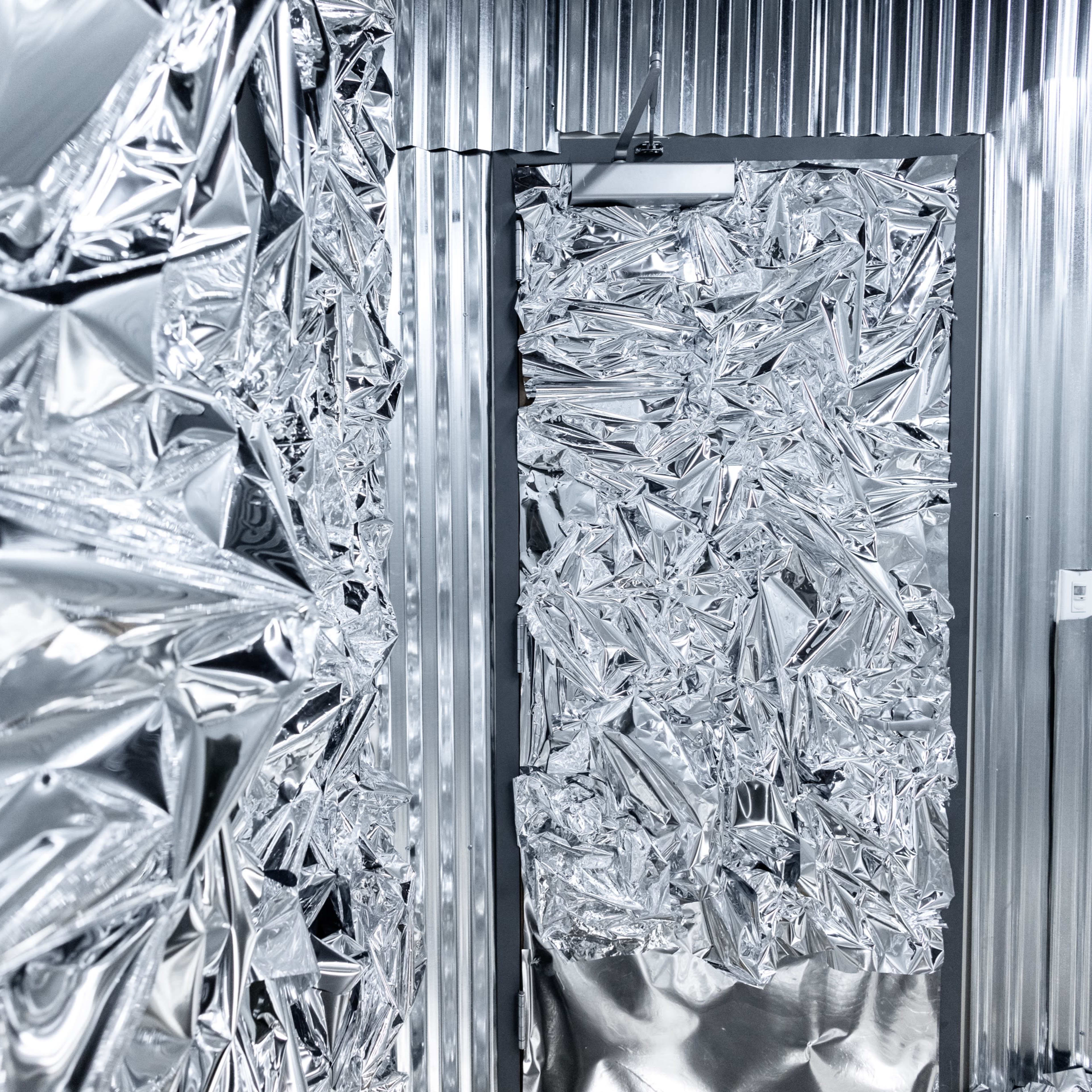 A hallway features walls and a door covered in crumpled, shiny metallic foil.
