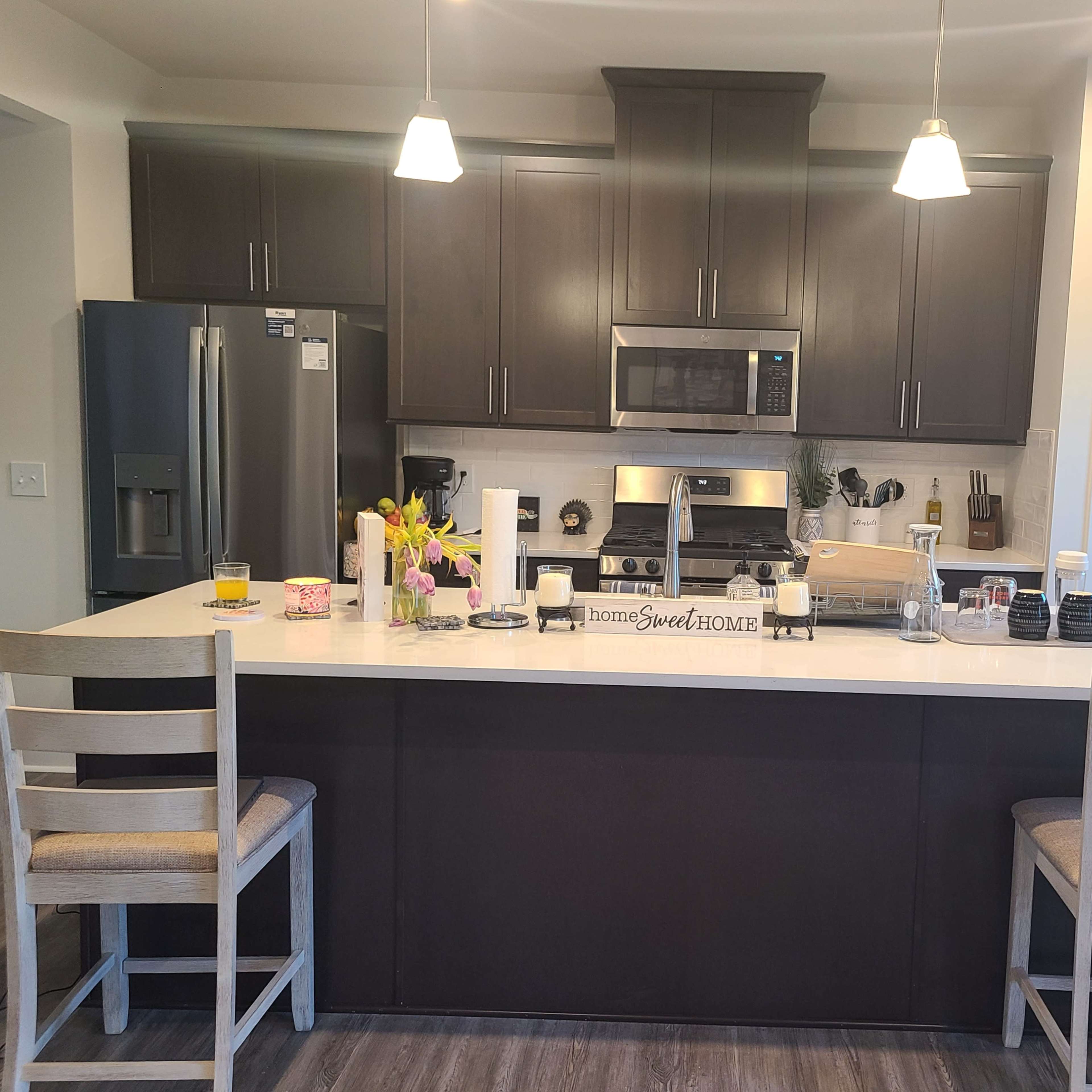 A modern kitchen featuring dark cabinetry, a central island with two chairs, and stainless steel appliances.