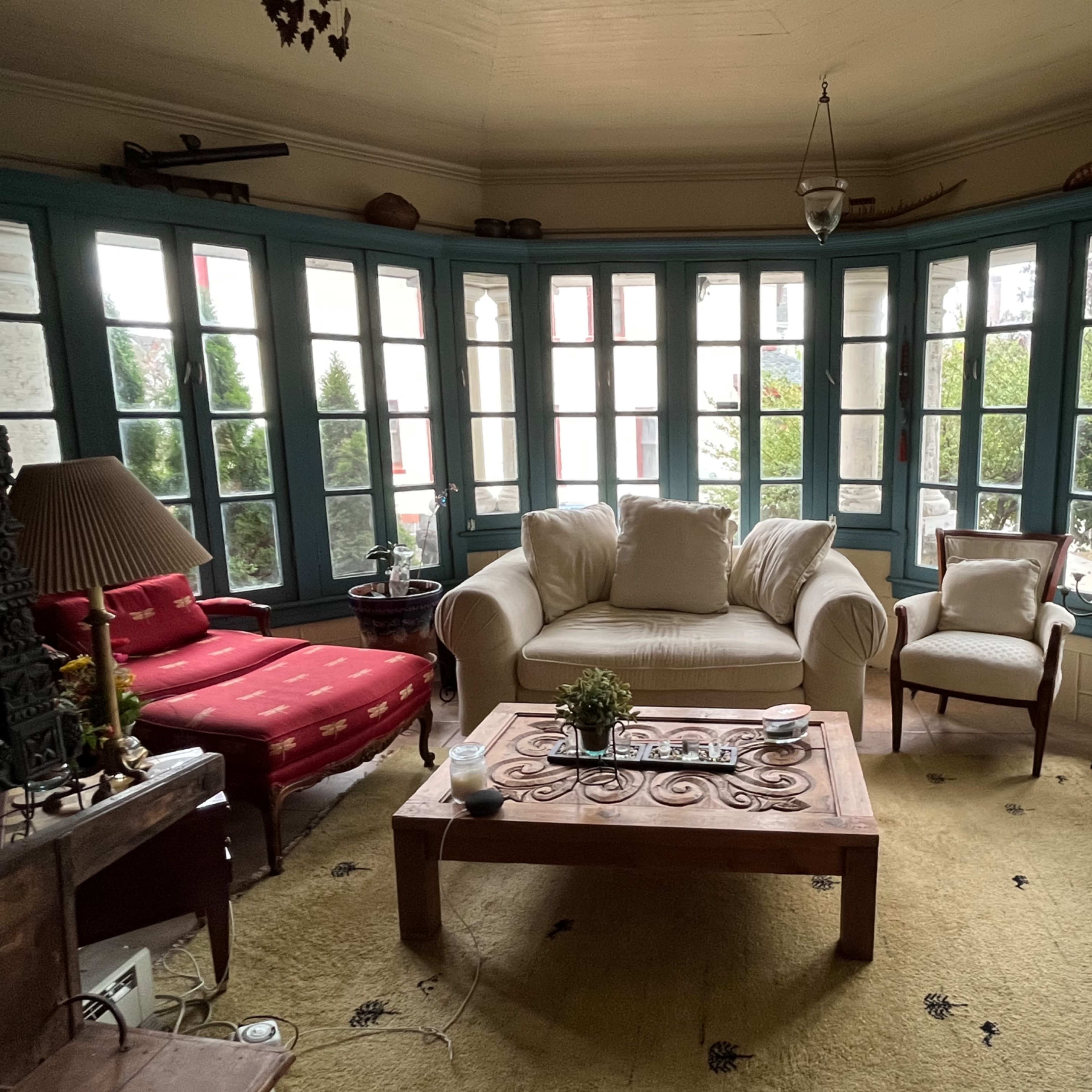 A cozy sunroom with large windows, a wooden coffee table, and several armchairs arranged around a central seating area.
