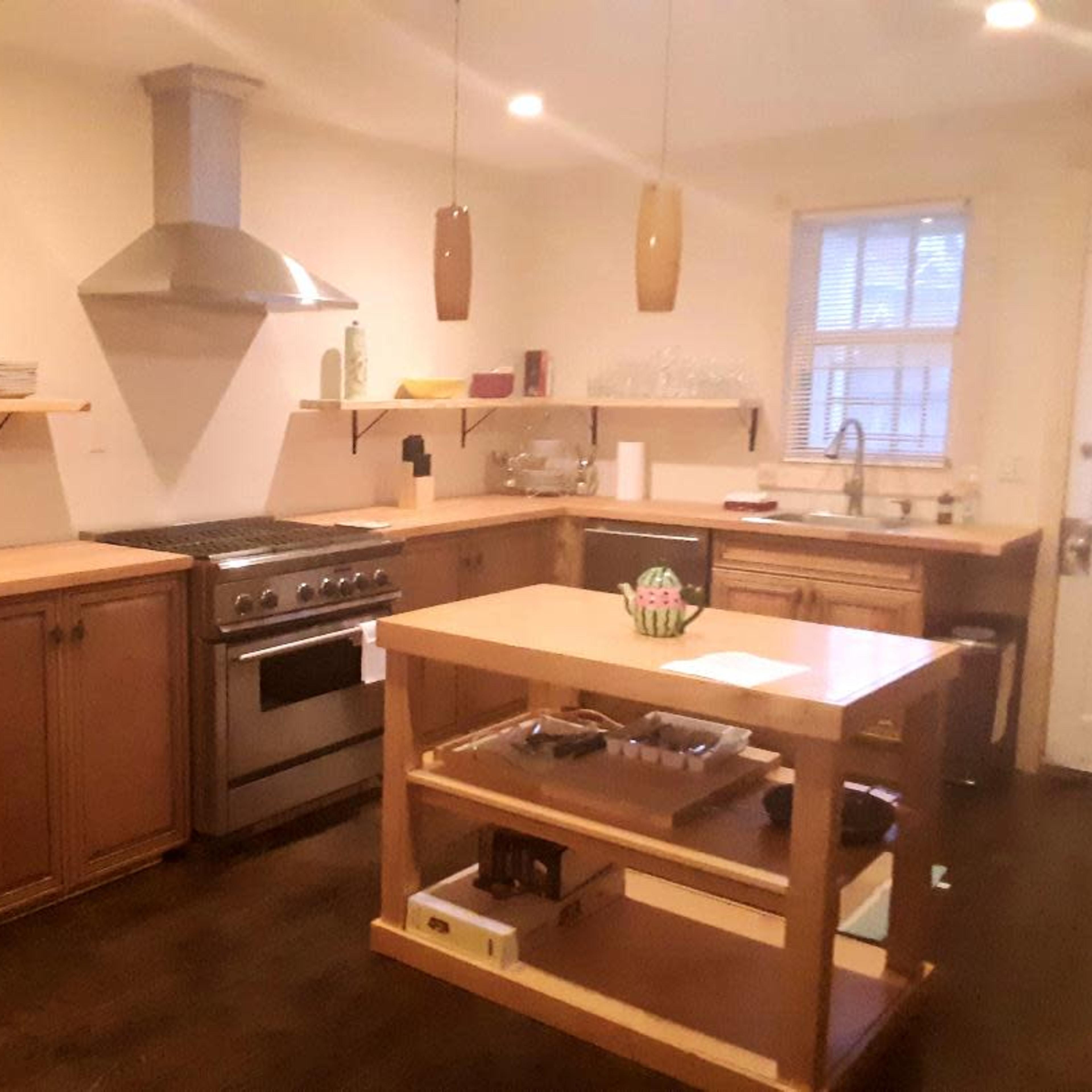 A modern kitchen with wooden cabinets, a stainless steel stove, and an island with open shelving.