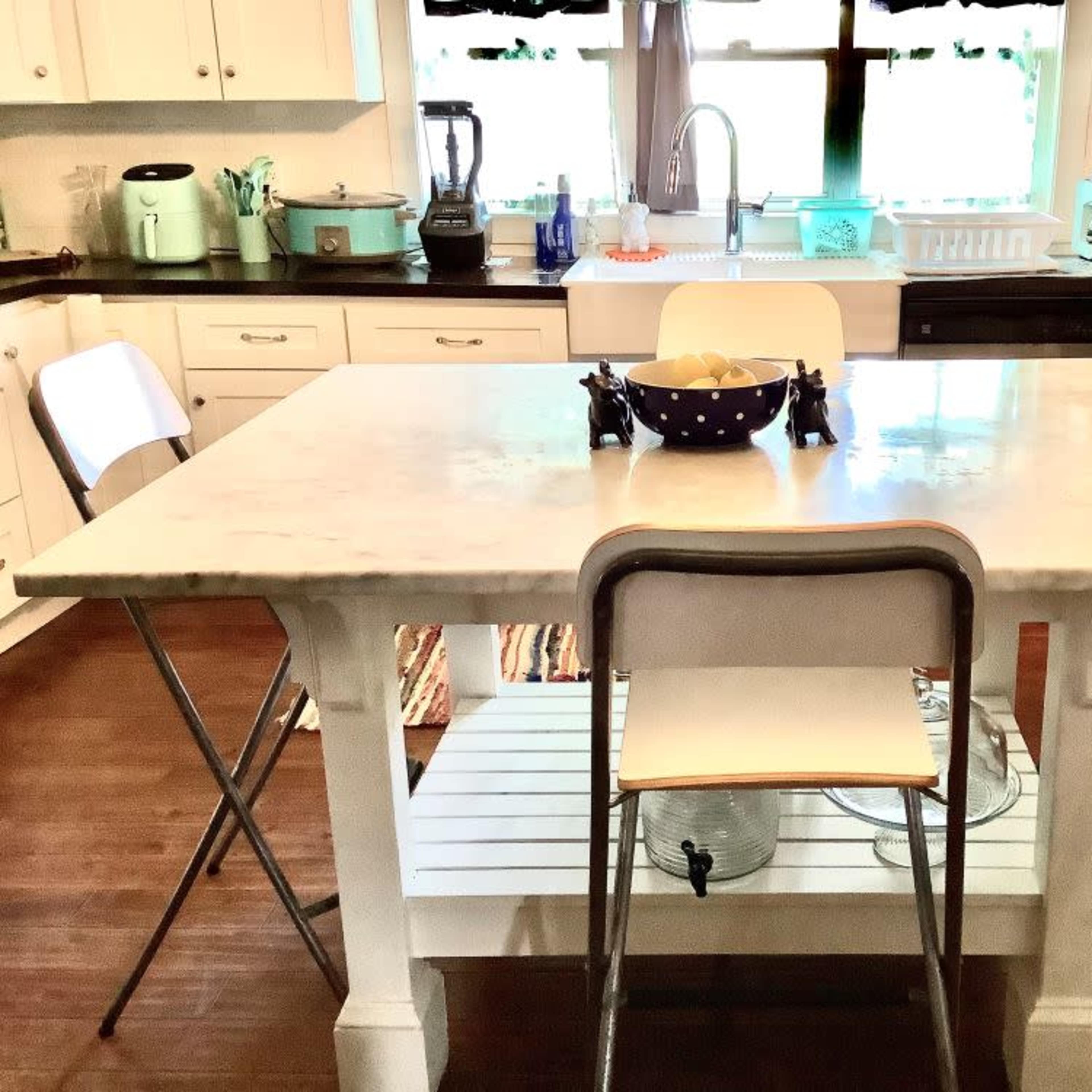 A kitchen featuring a marble-topped table with two folding chairs, surrounded by white cabinetry and various appliances.
