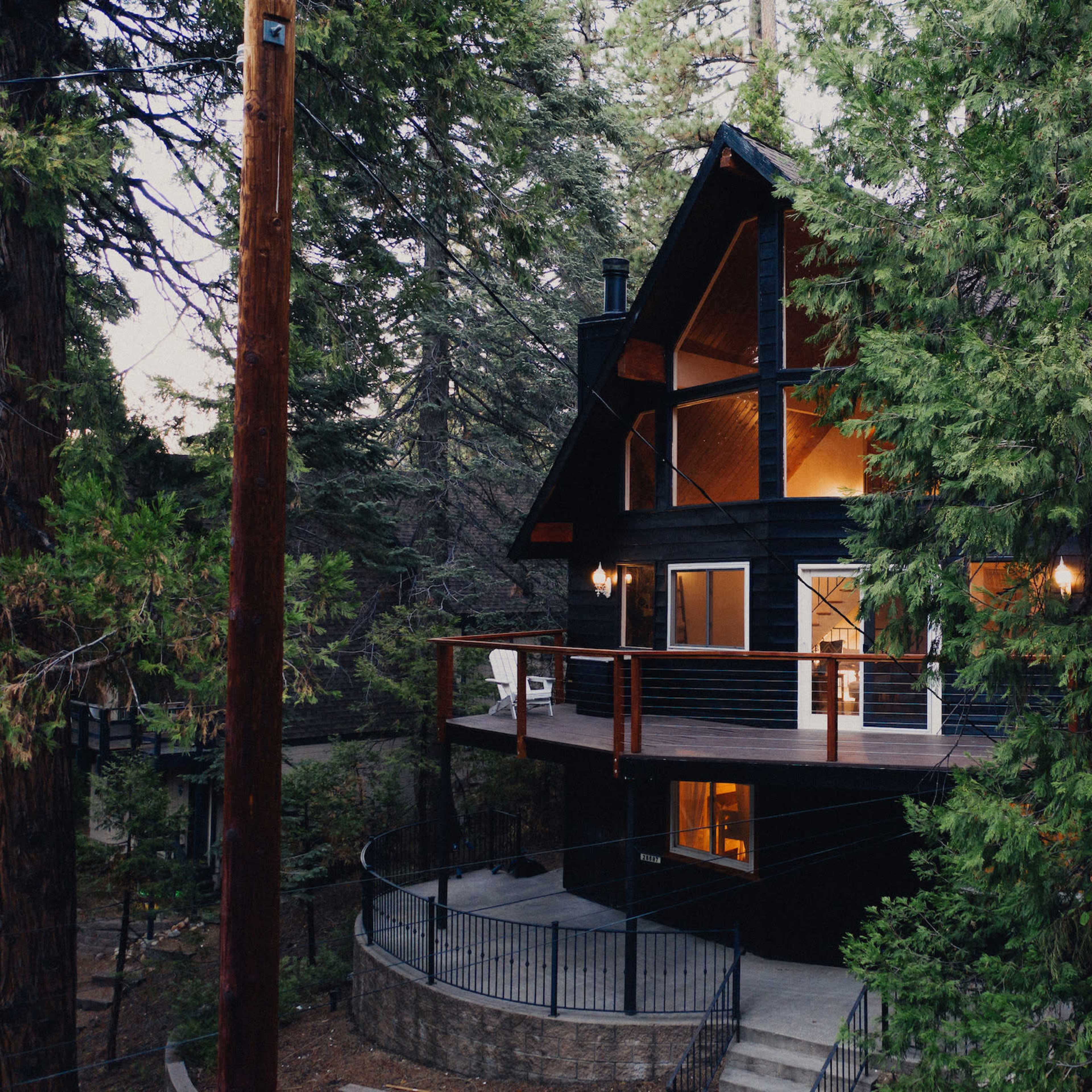 A black wooden cabin with a balcony is nestled among tall green trees.