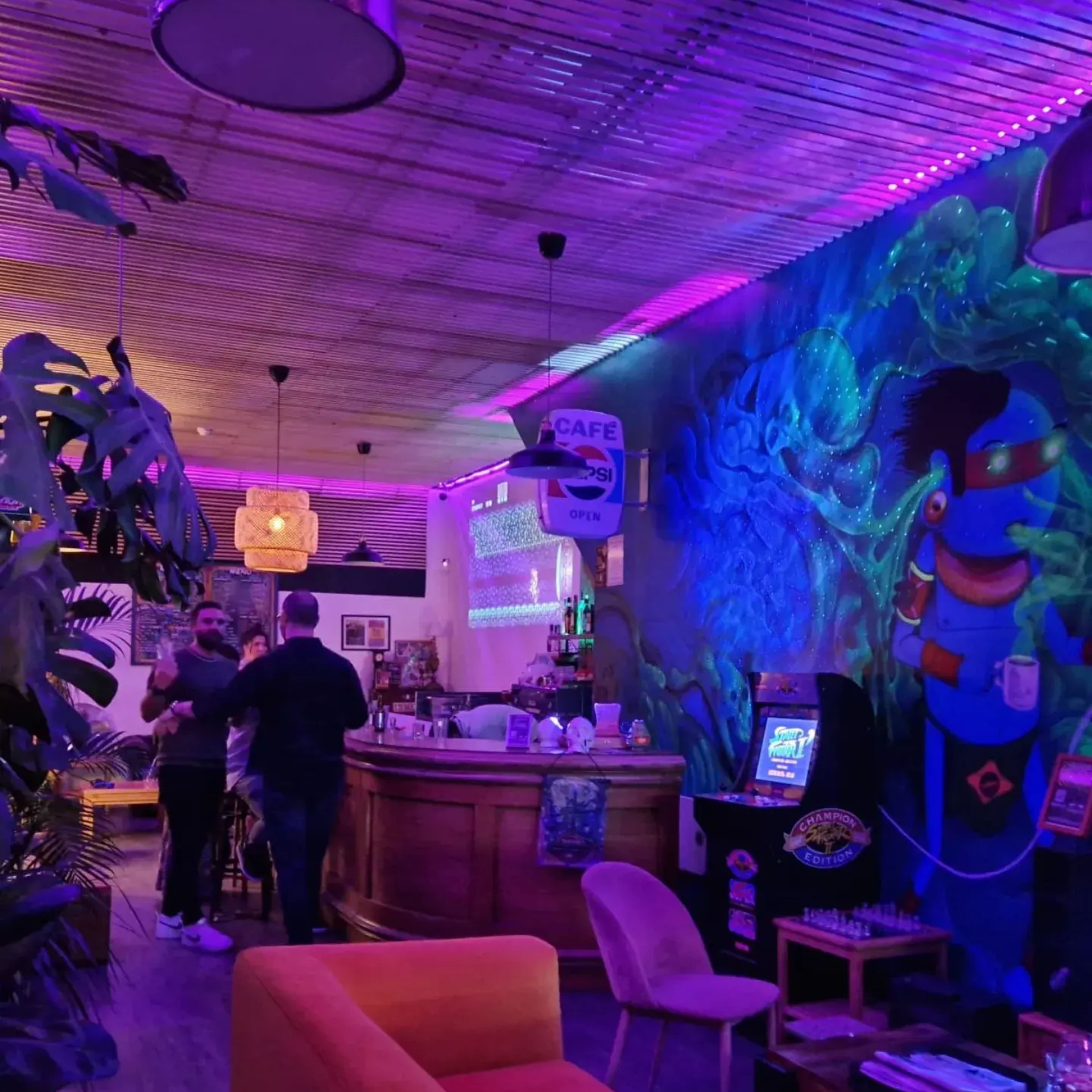 A bar area features vibrant wall art and colorful lighting, with customers gathered near the counter and seating arranged nearby.