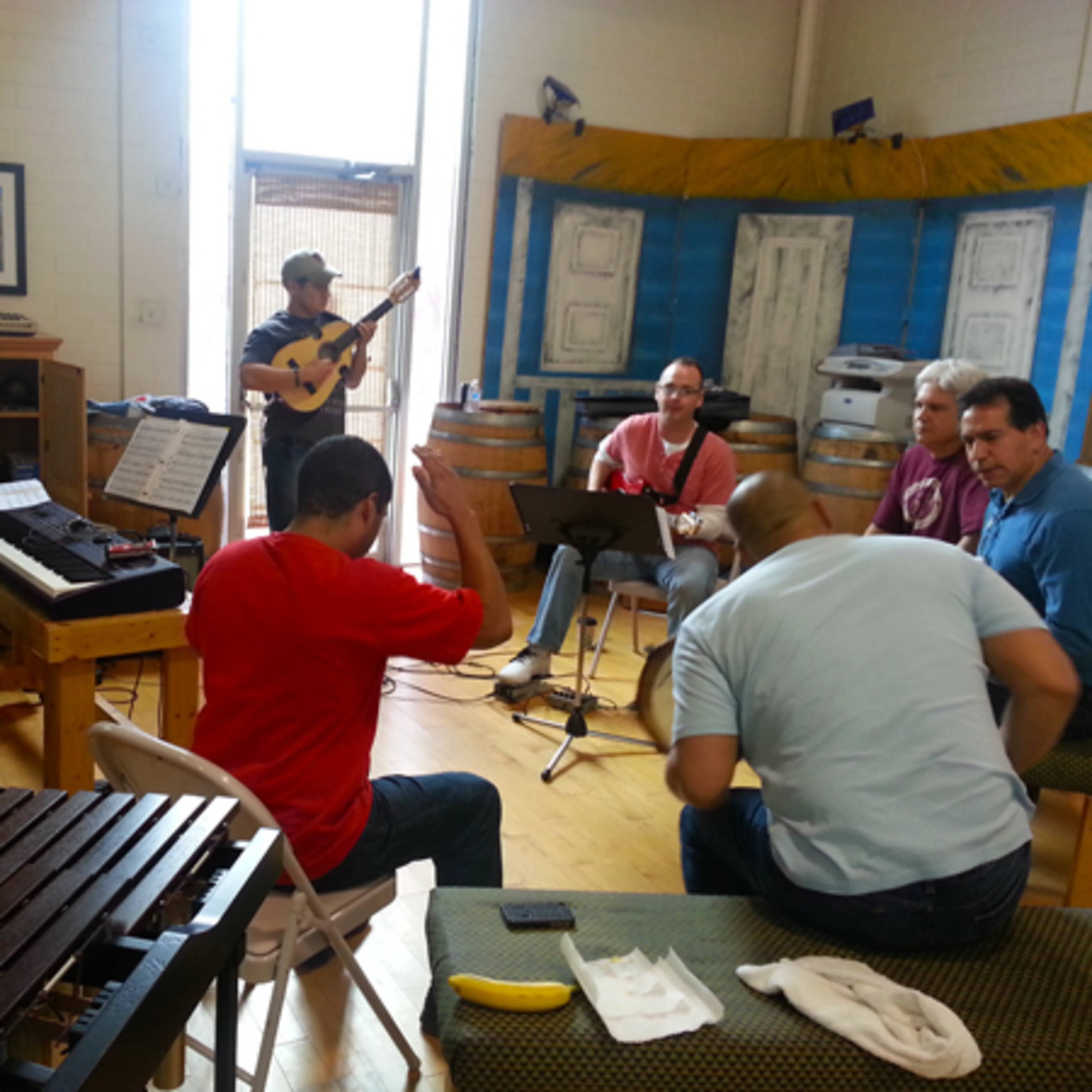A group of musicians is gathered in a room, playing various instruments, while some are seated and engaged in conversation.