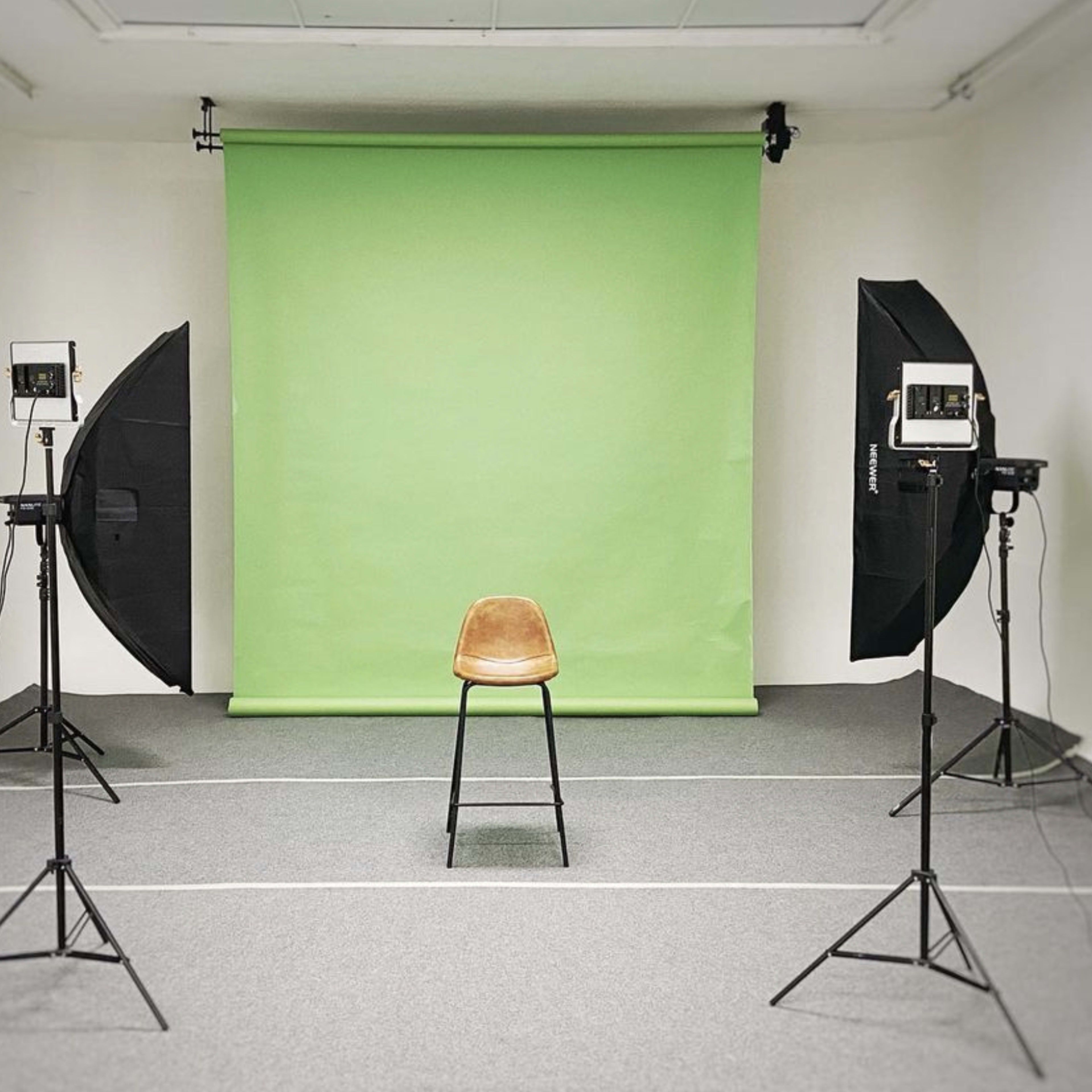 A studio setup featuring a single brown chair in front of a green backdrop, flanked by two large light softboxes on stands.