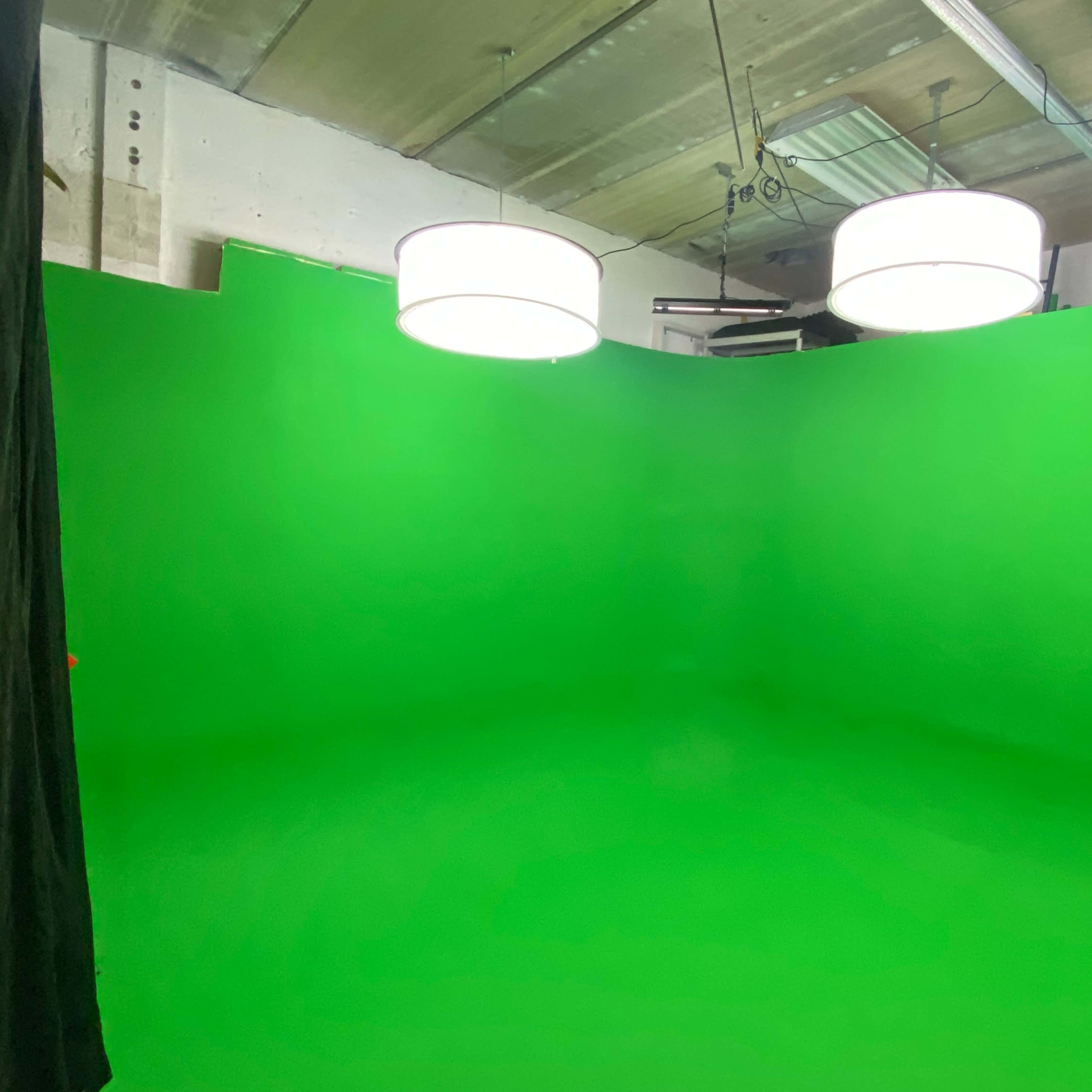 A green screen studio with three round pendant lights hanging from the ceiling.