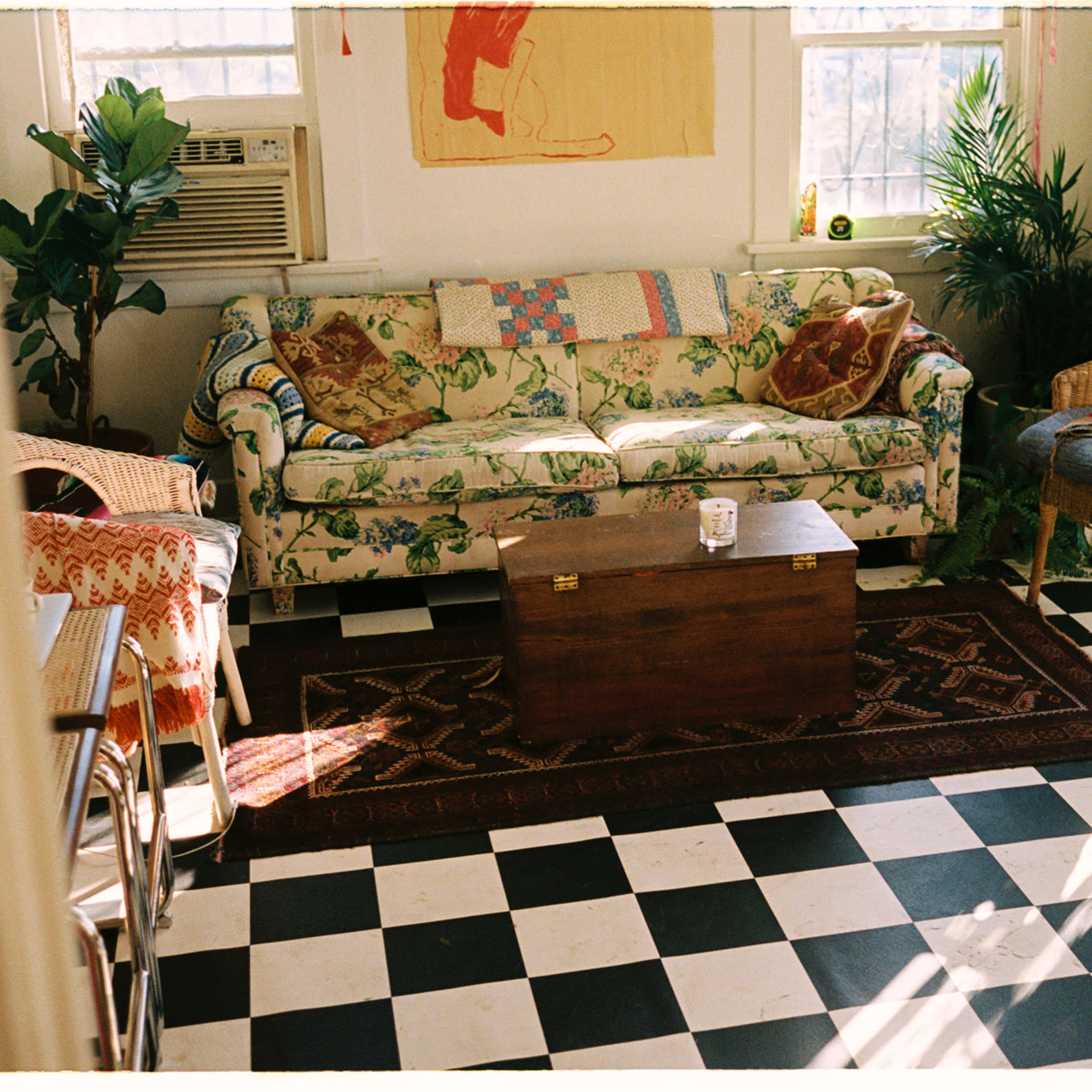 A cozy living room featuring a patterned couch, a wooden coffee table, and various armchairs arranged around a checkered floor.