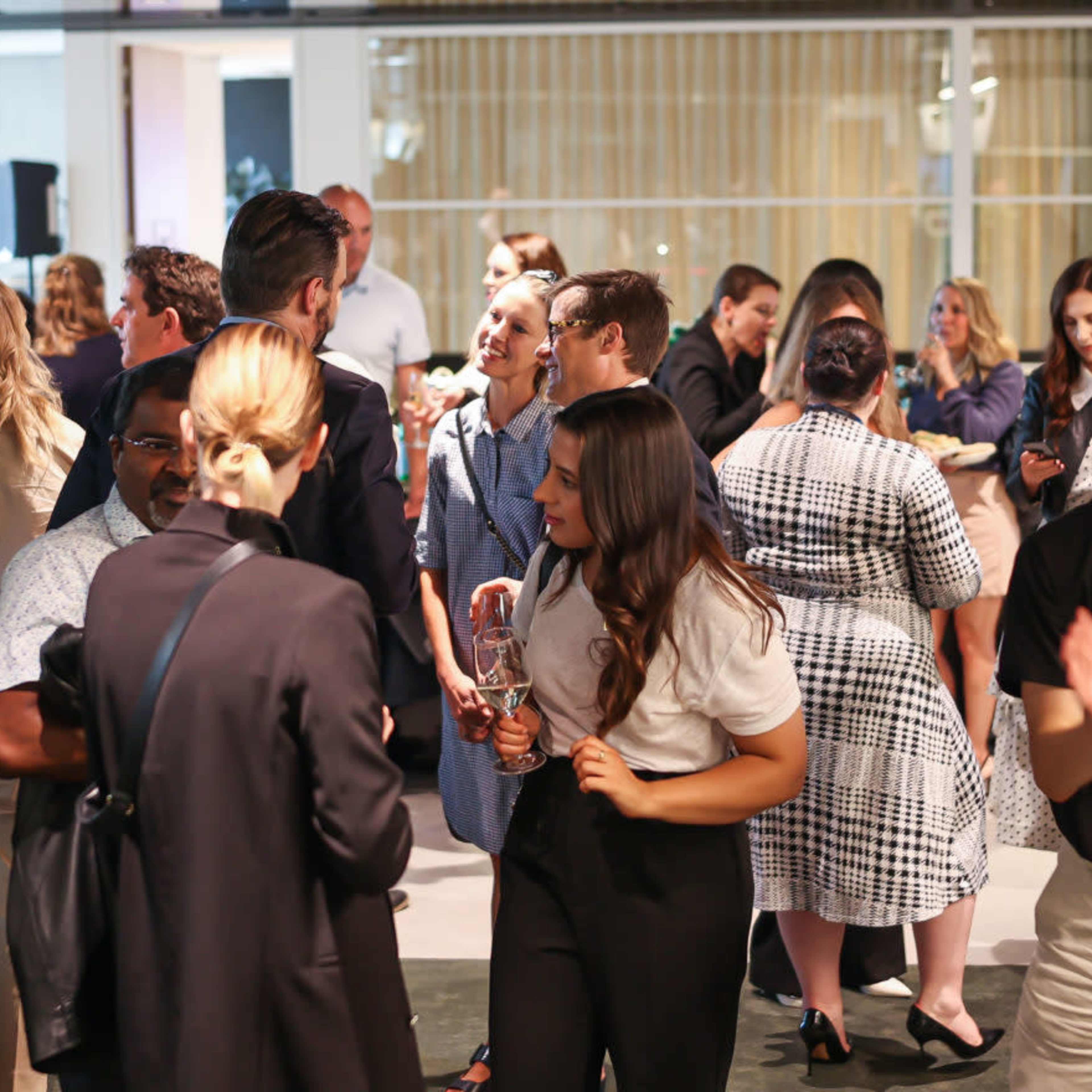 A large group of people socialize at a networking event in a modern indoor space.