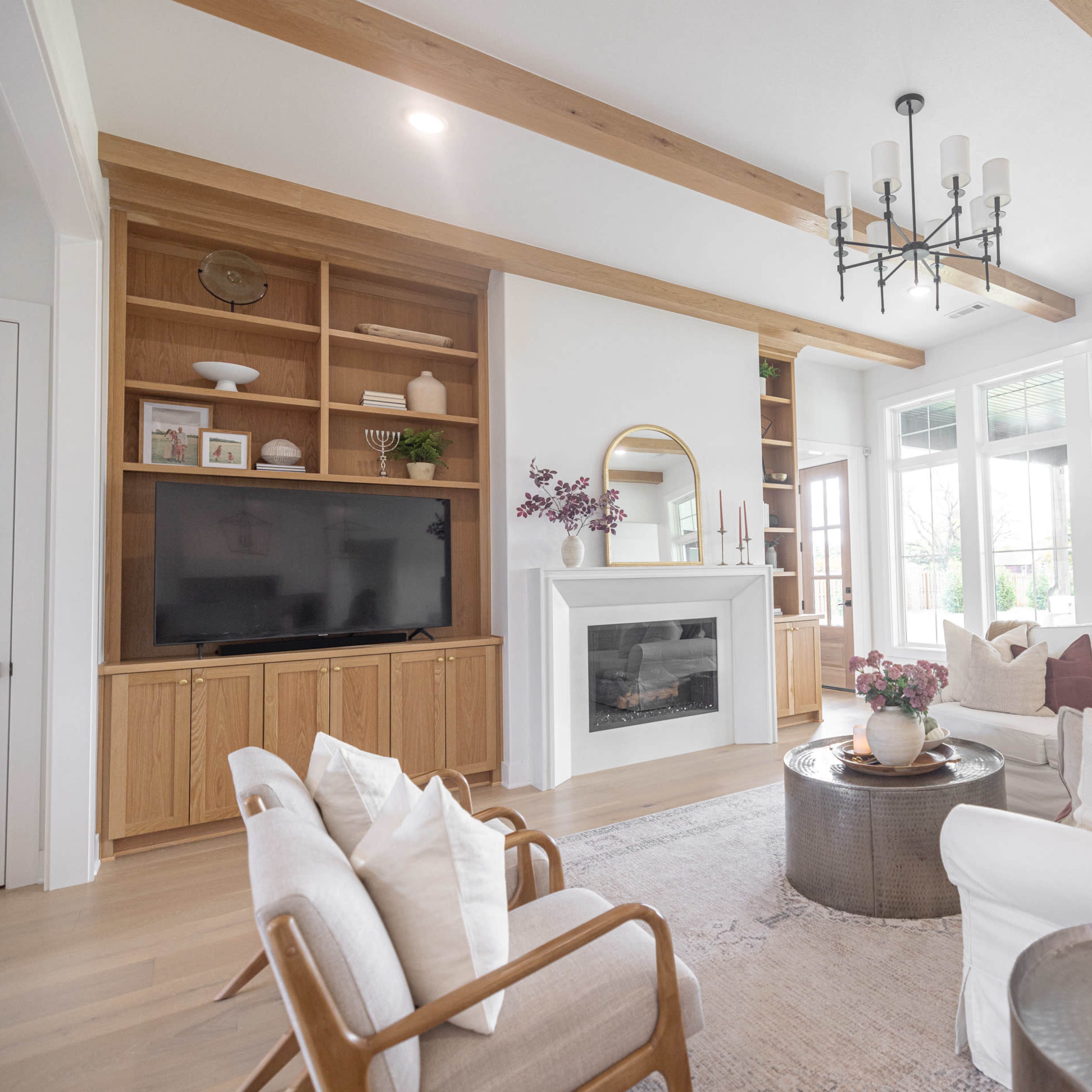 A modern living room with a fireplace, built-in shelving, large windows, and a comfortable furniture arrangement.