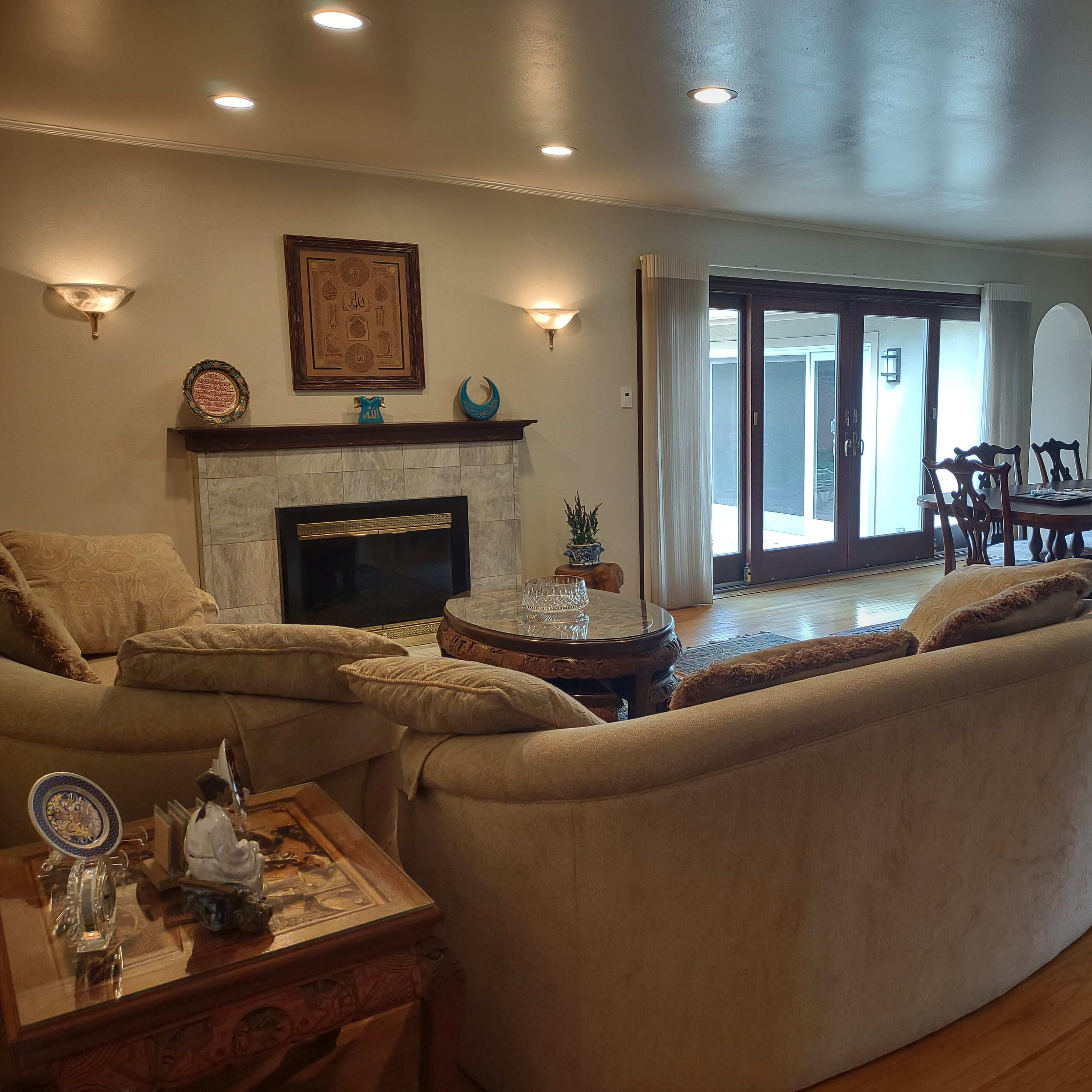A spacious living room with a beige sectional sofa, a fireplace, and a dining area featuring a wooden table and a glass-front cabinet.