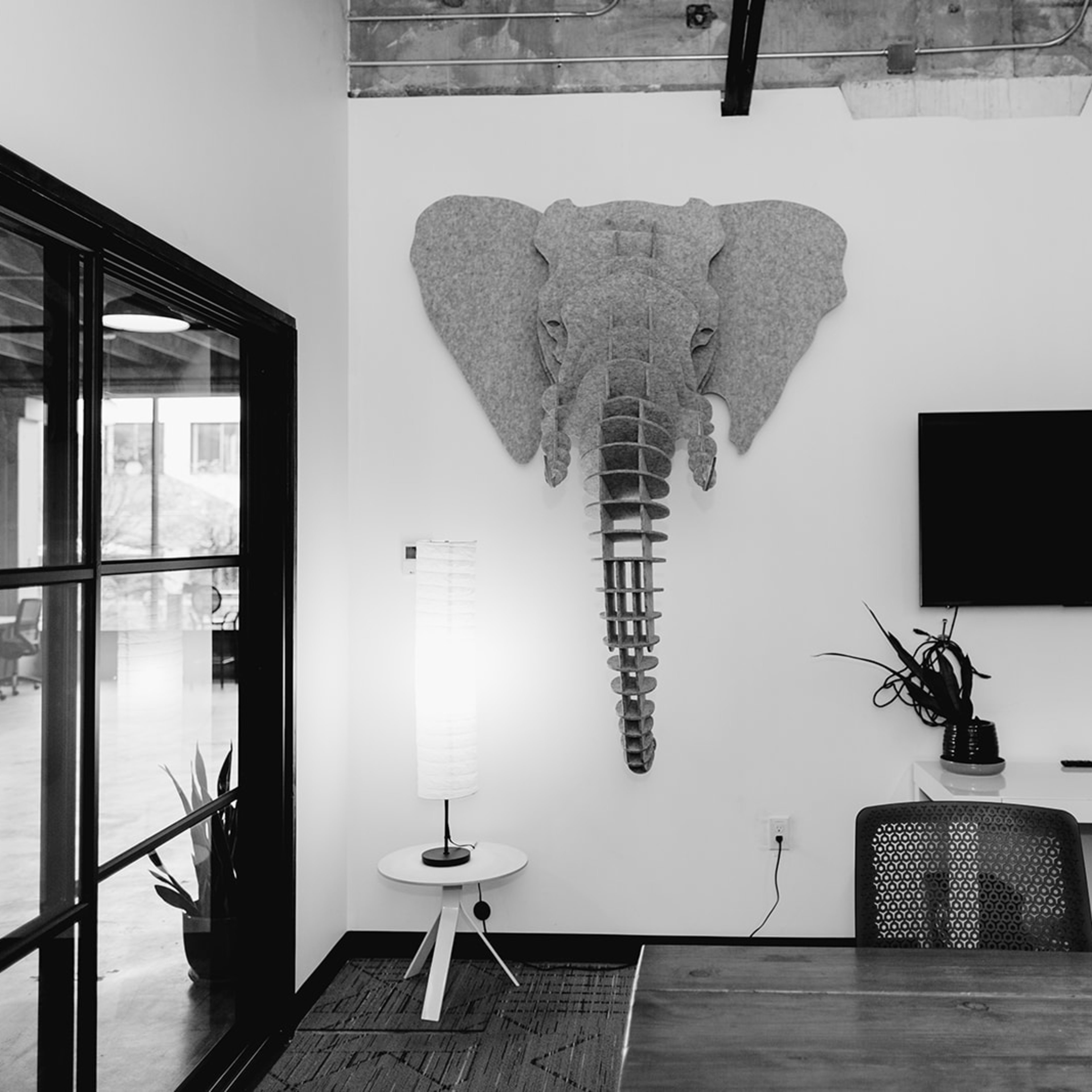 An office space featuring a wall-mounted elephant sculpture, a television, a lamp, and a table with chairs.