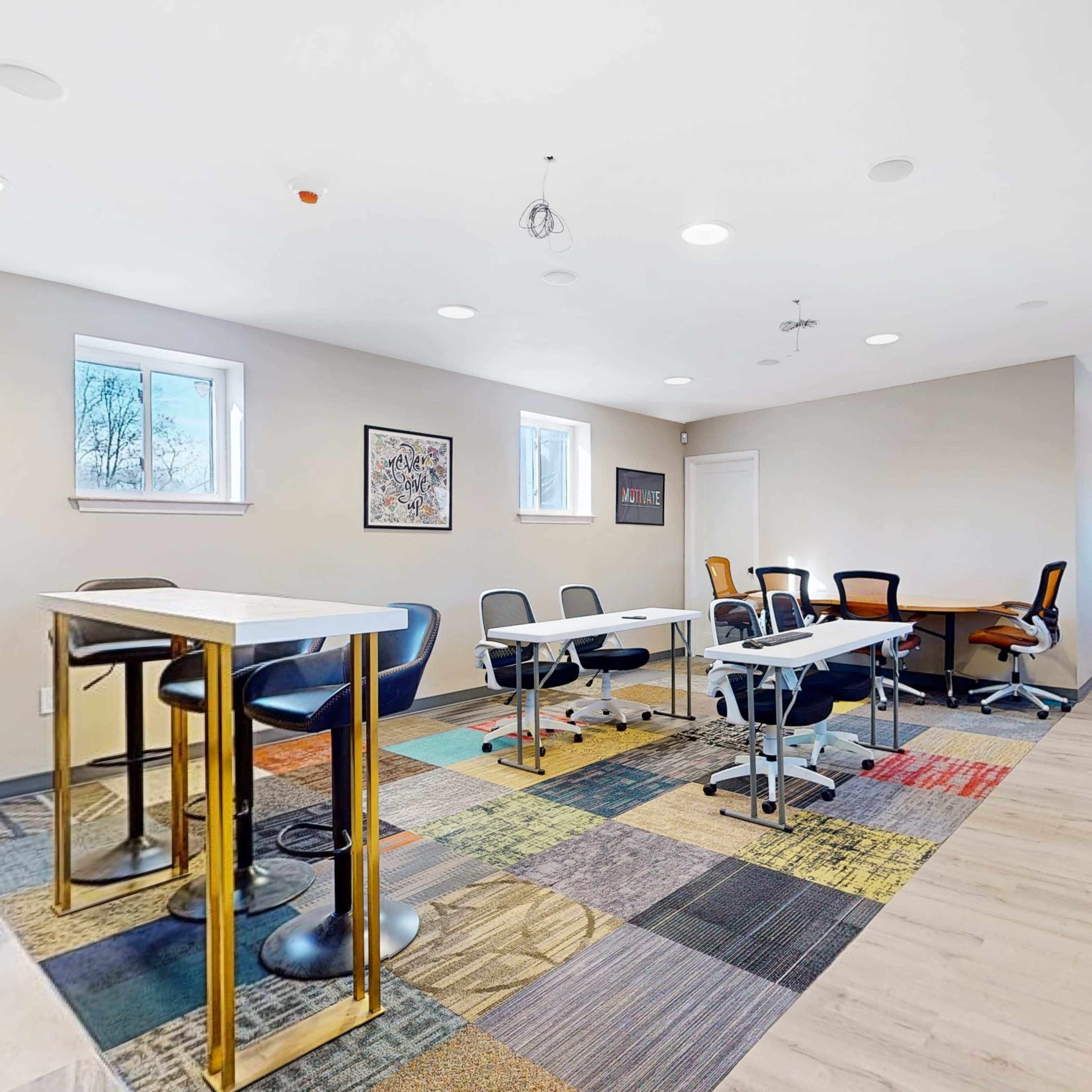 A modern office space with several tables, chairs, and a large screen on one wall.