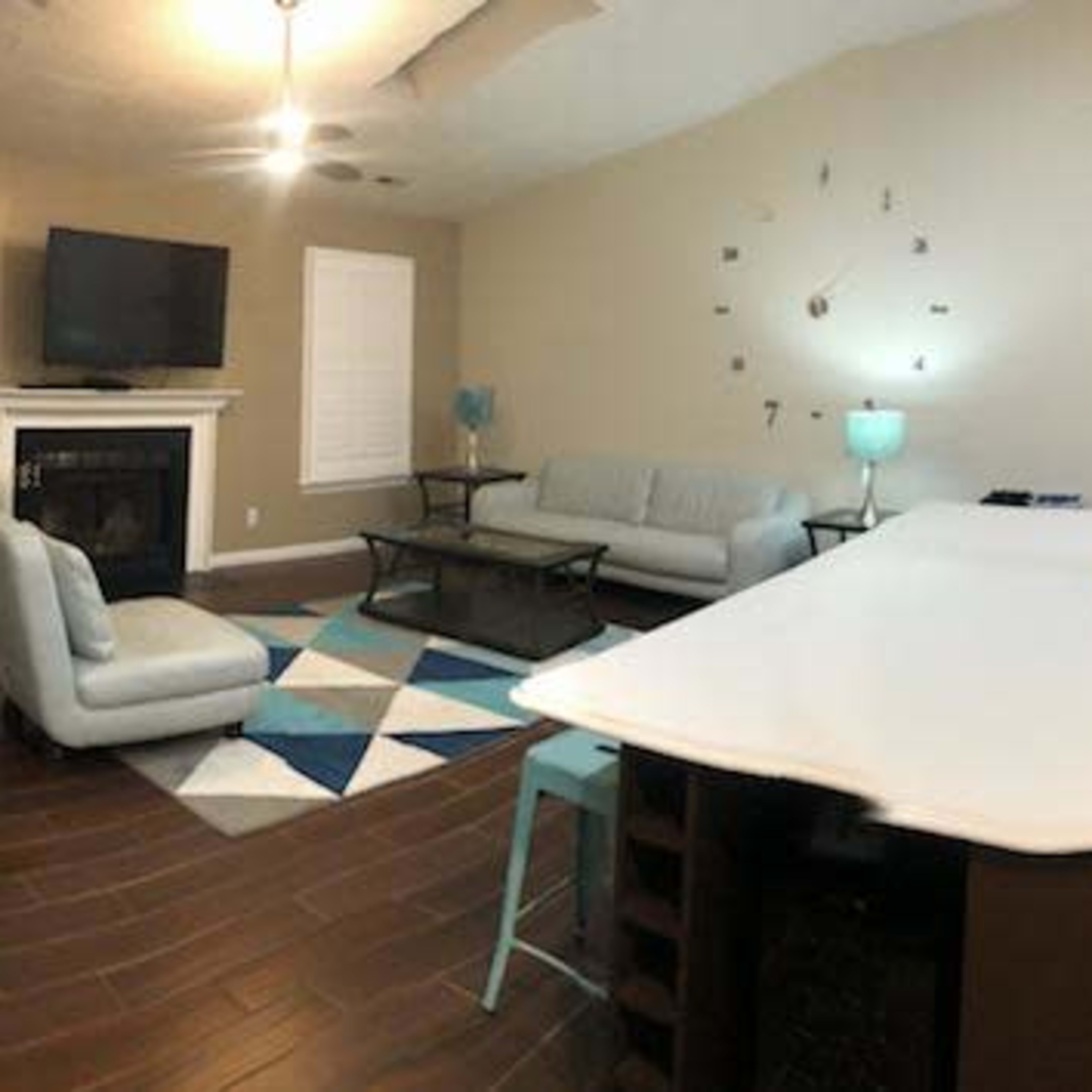 A panoramic view of a modern, open-concept living space featuring a kitchen island, dining table, and seating area with a television.