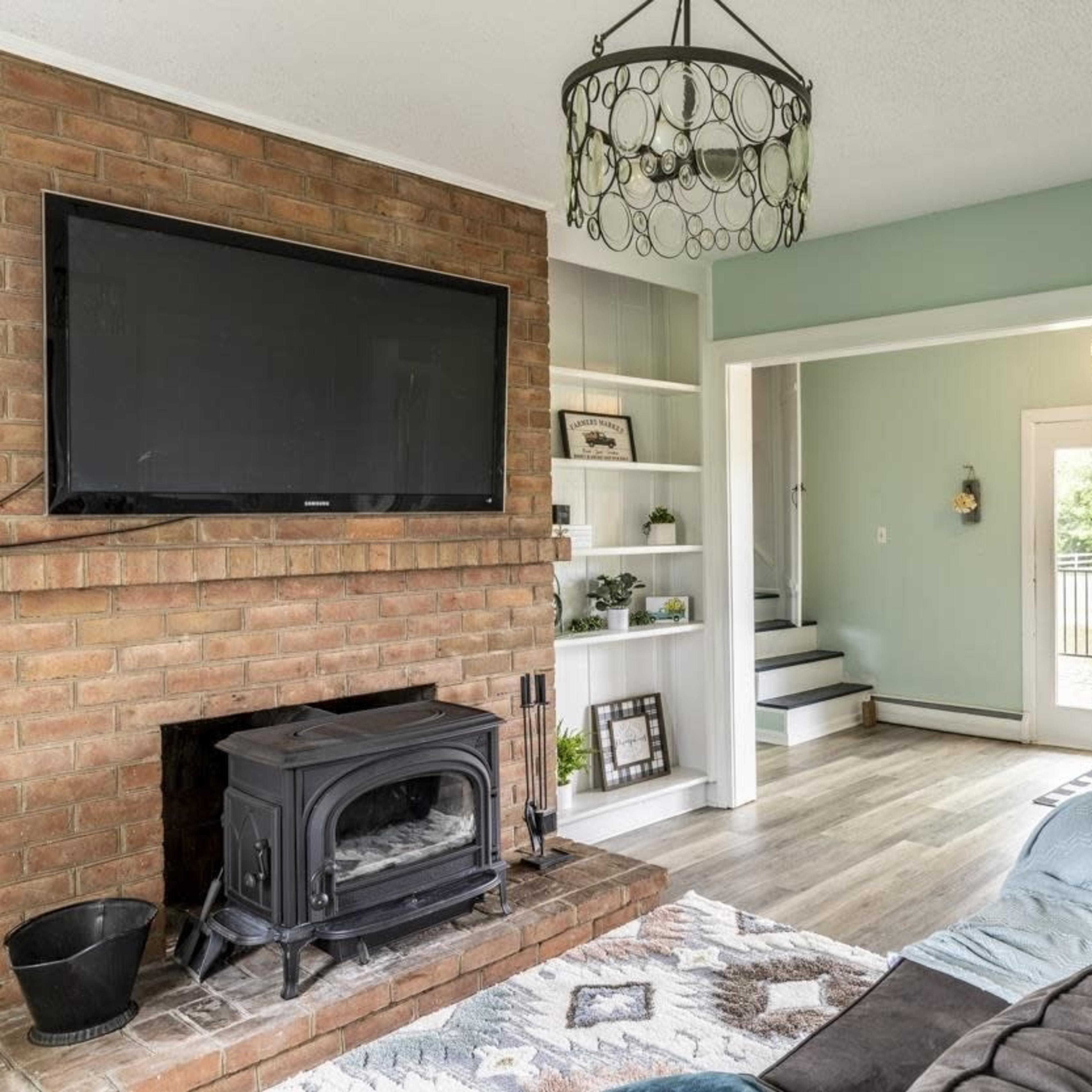A living room with a brick fireplace, a mounted television, and a set of large glass doors leading to an outdoor area.
