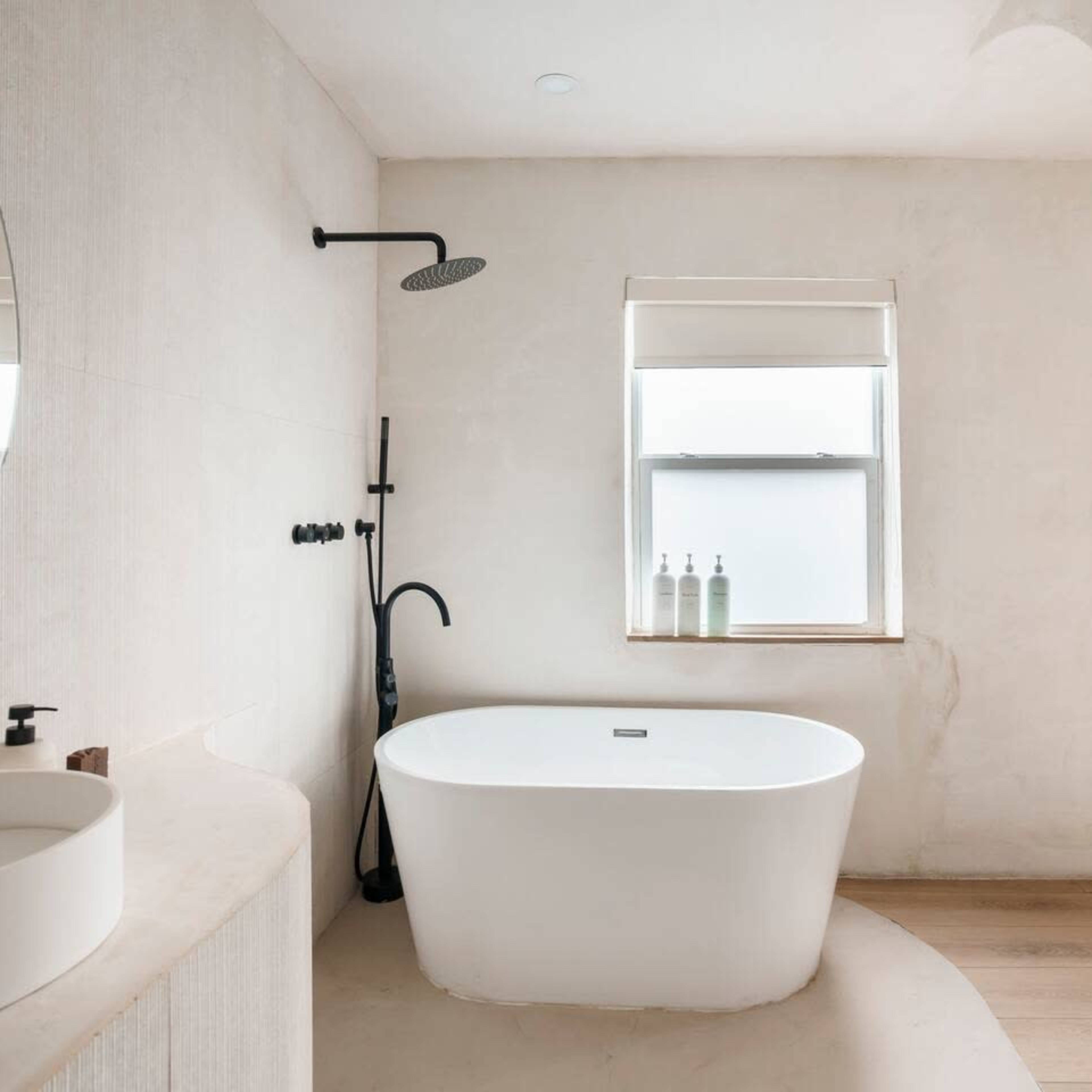 A modern bathroom featuring a freestanding bathtub, a round mirror, and a window with natural light.