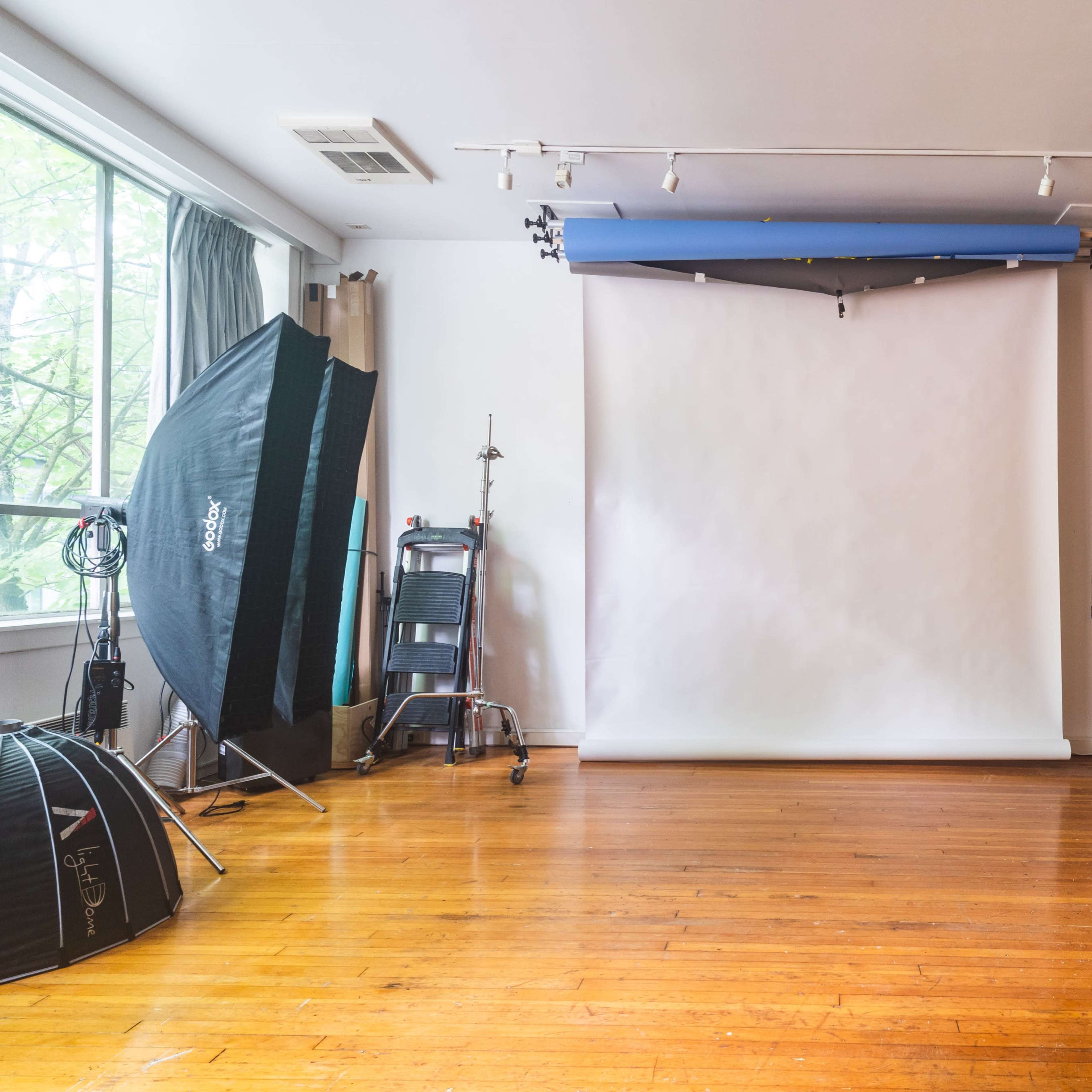 A spacious studio with hardwood floors features a white backdrop setup and various photography equipment along the walls.