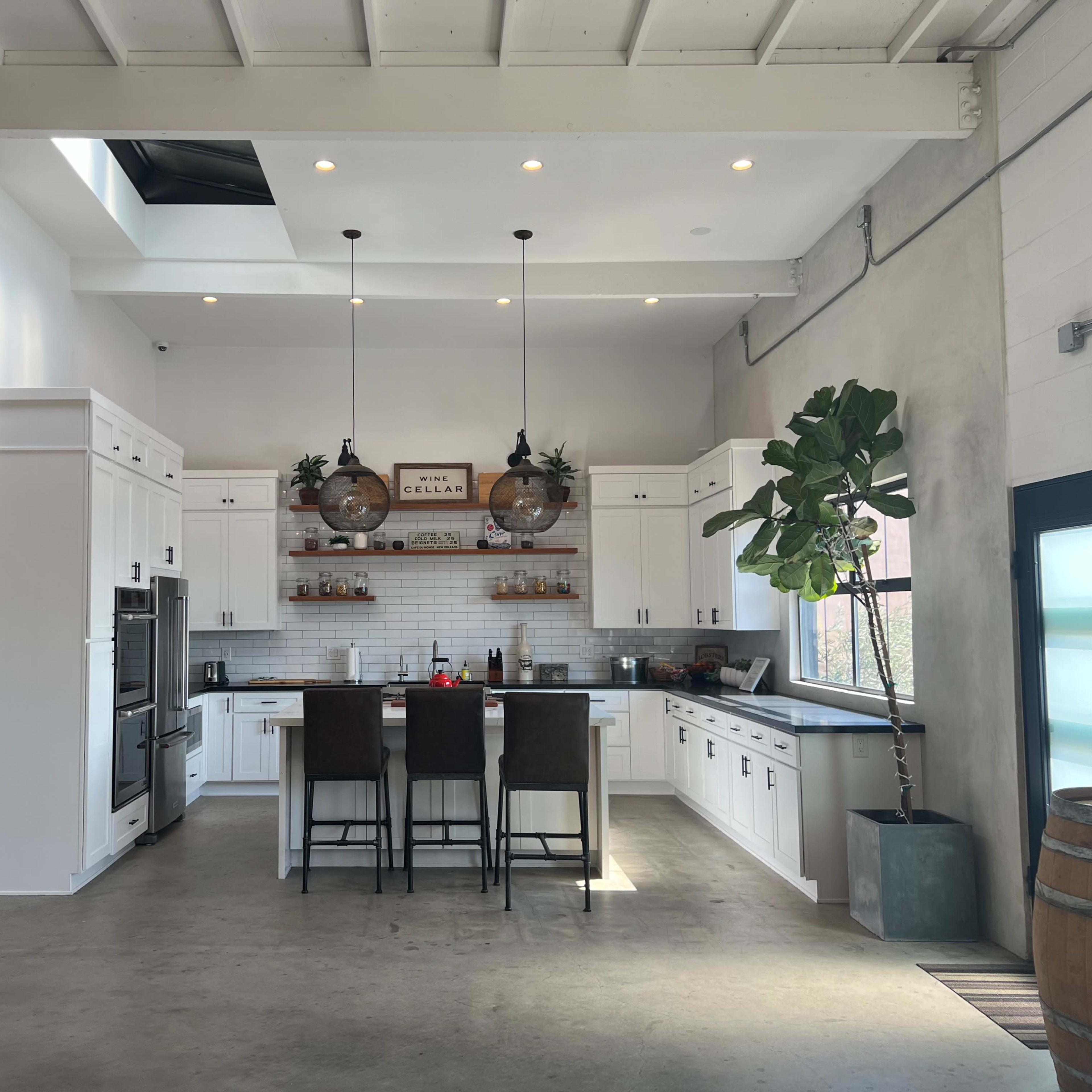 A modern kitchen with white cabinetry, a central island with bar stools, and large windows allowing natural light to fill the space.