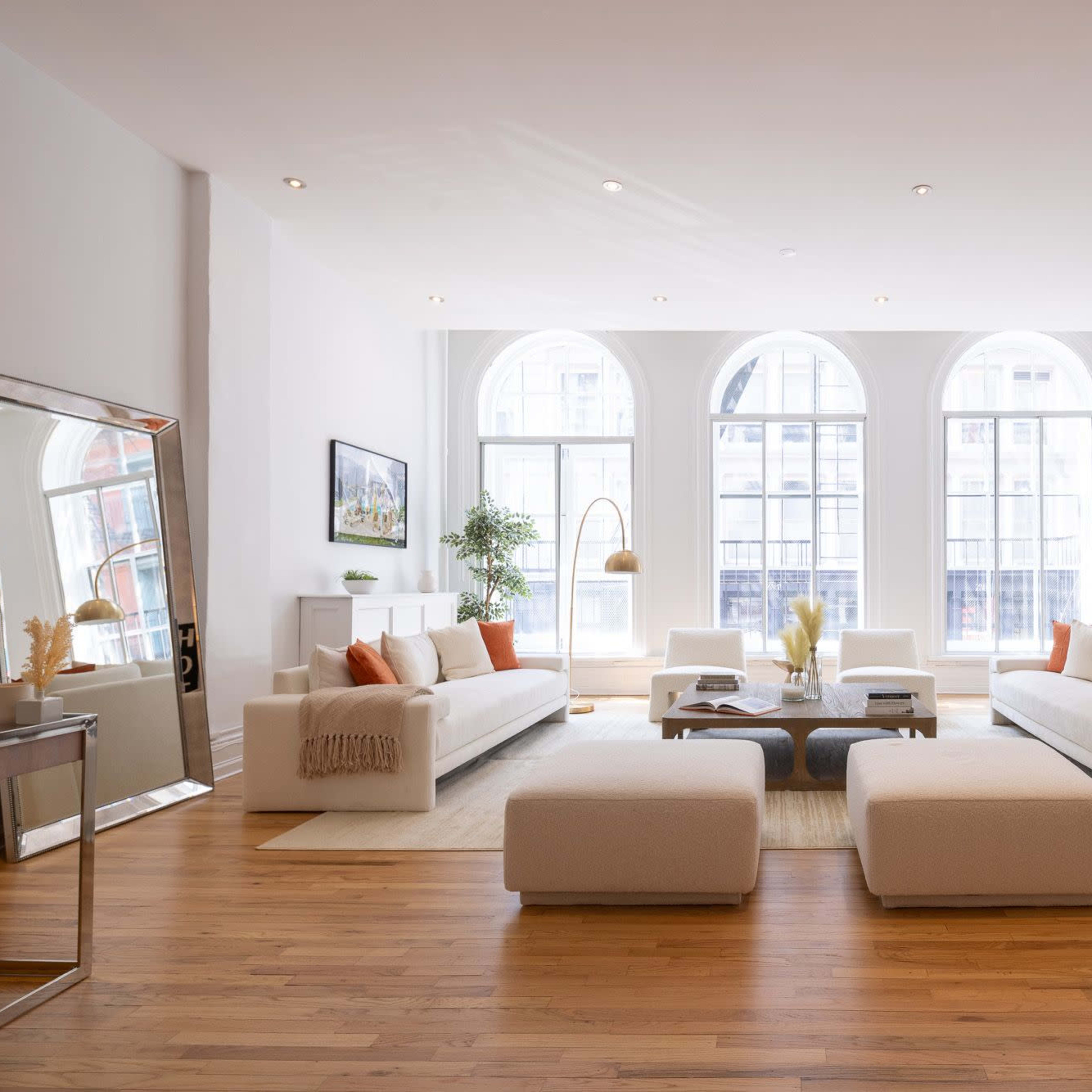 A spacious living room with large arched windows, two white sofas, a coffee table, and decorative elements including plants and artwork.