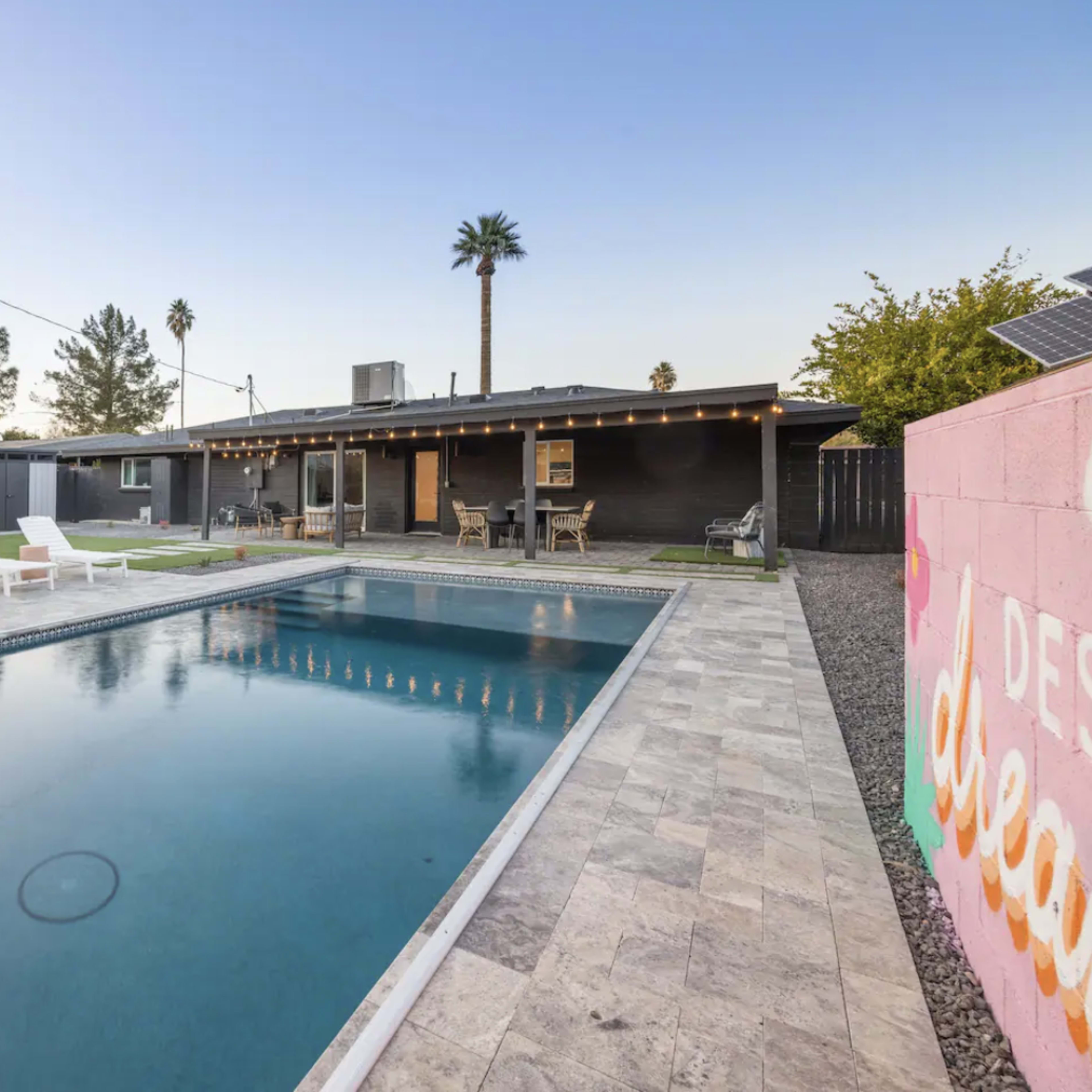 A backyard with a swimming pool, lawn chairs by a swimming pool, and a modern house in the background.