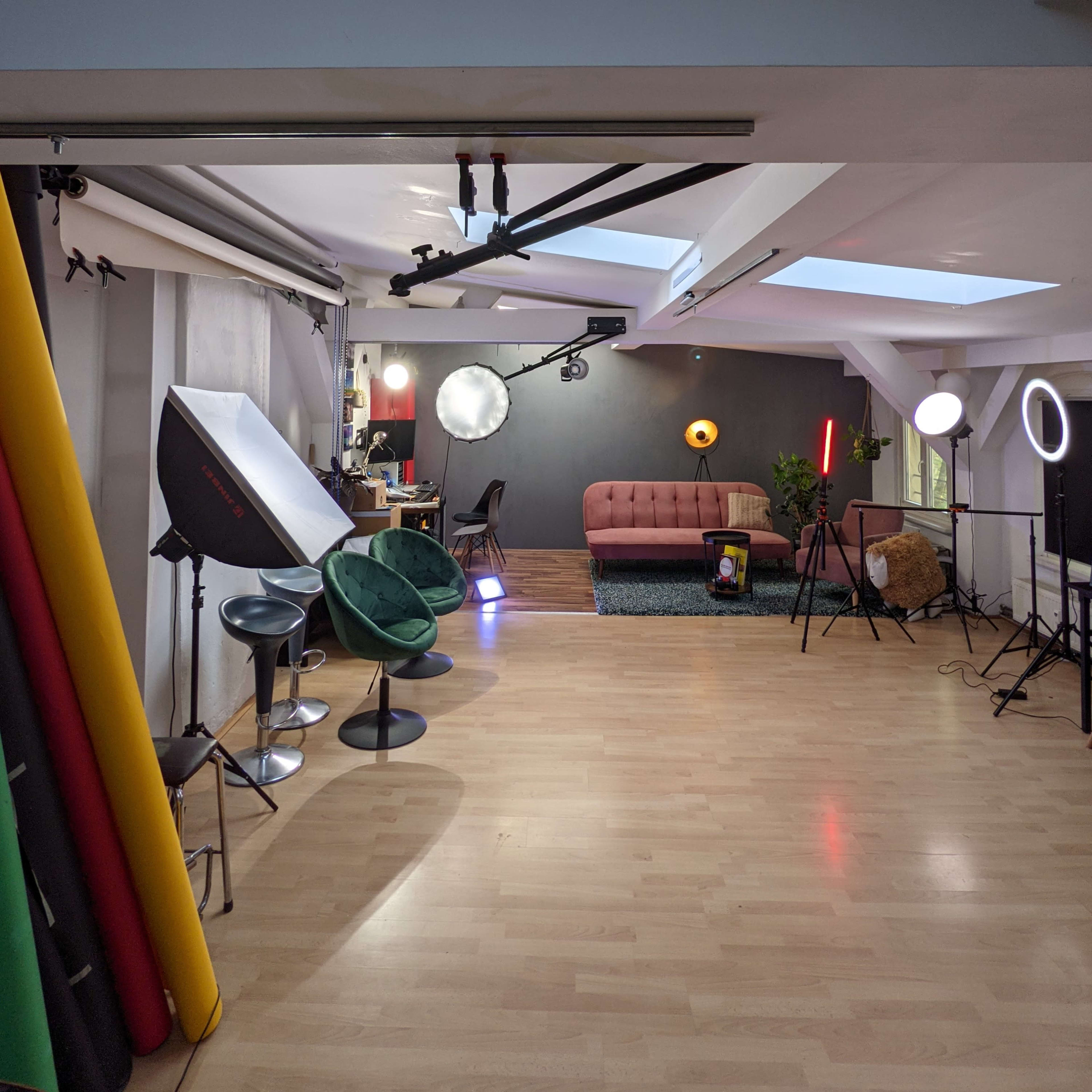 A photography studio with various lighting equipment, a red sofa, and colorful backdrop rolls on one side.