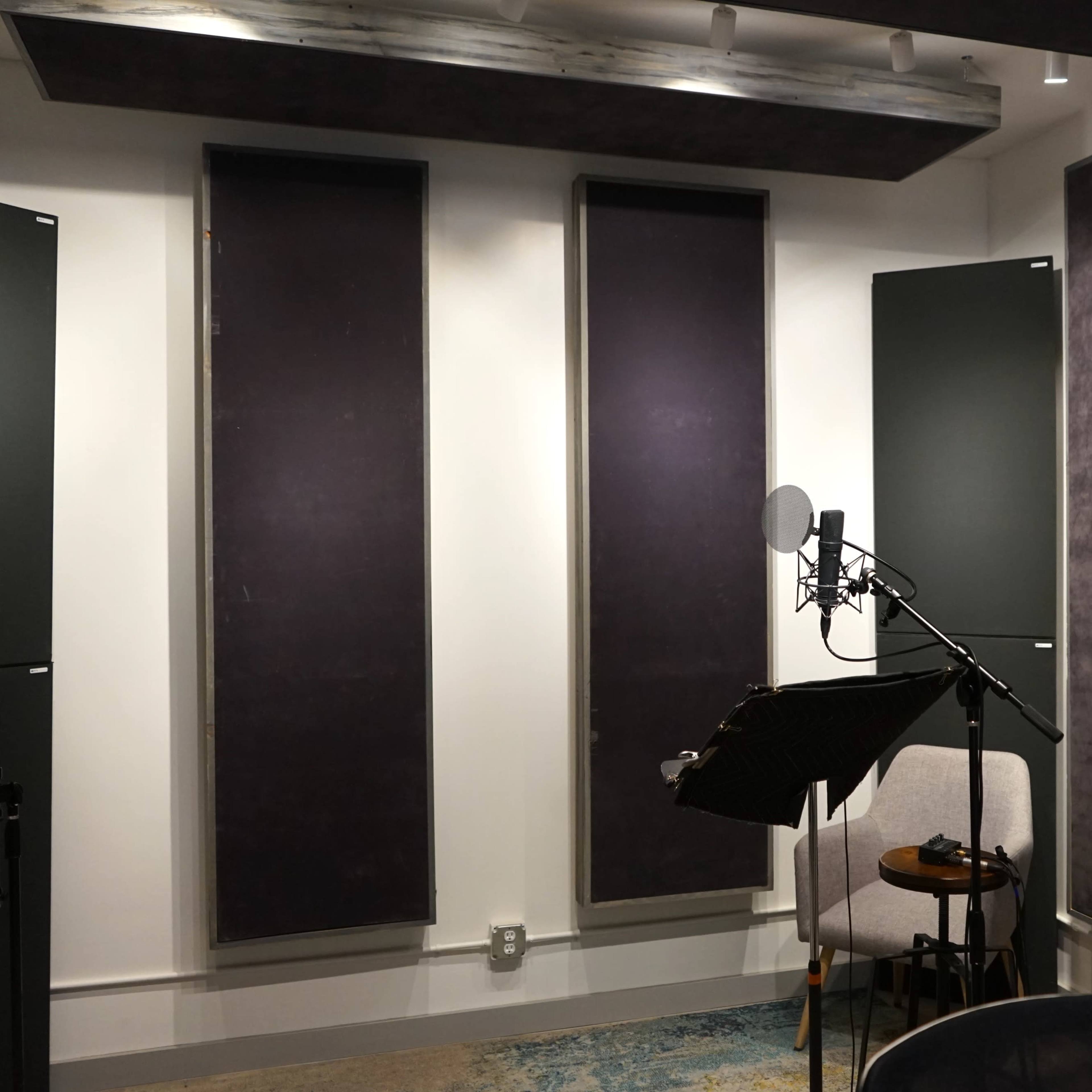 A sound recording studio with padded wall panels, a microphone on a stand, a music stand, and a chair.