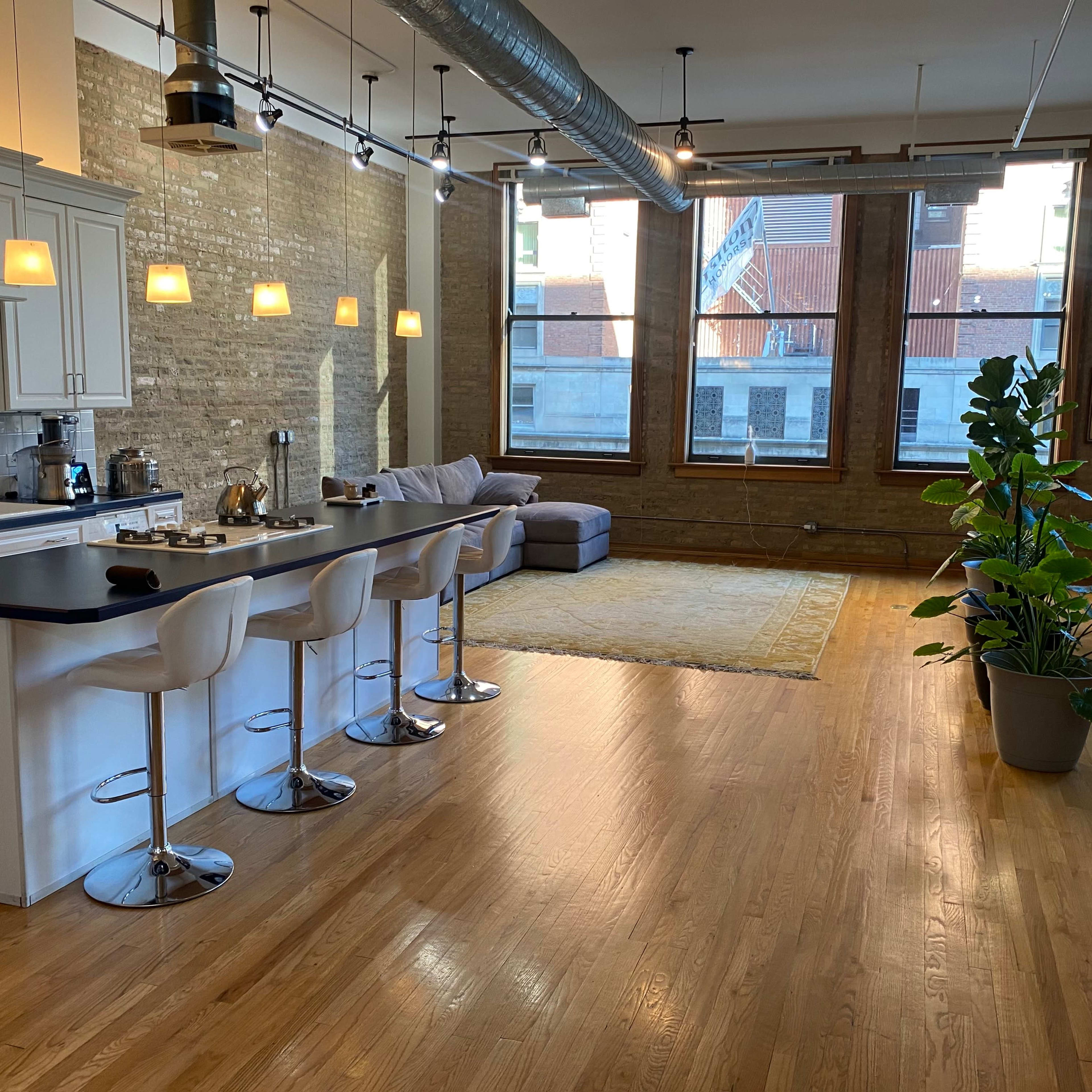 A spacious, modern apartment with a kitchen island and bar stools, a living area with a sofa, and large windows providing natural light.
