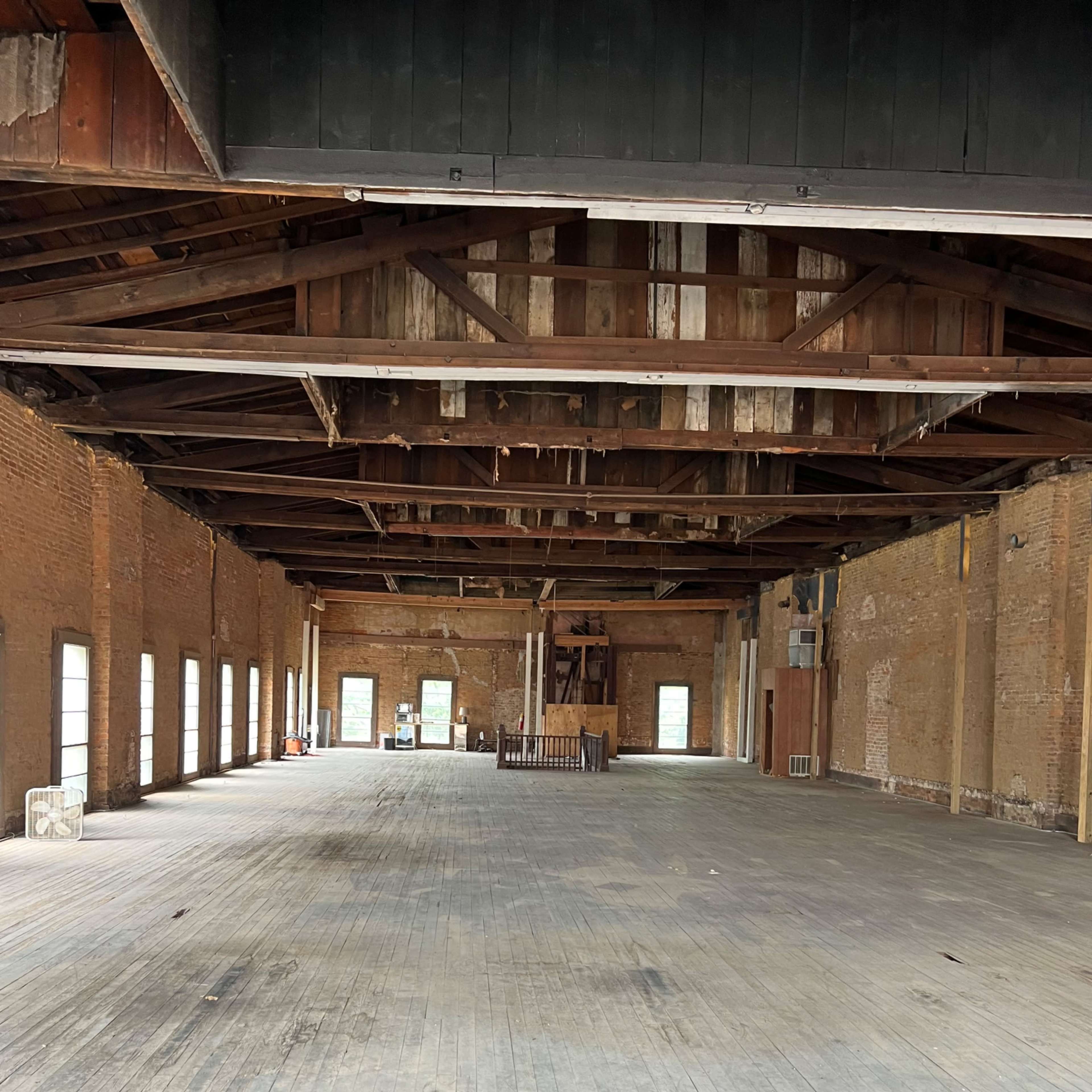 An empty, large interior space with wooden floors, exposed brick walls, and high wooden beams in the ceiling.