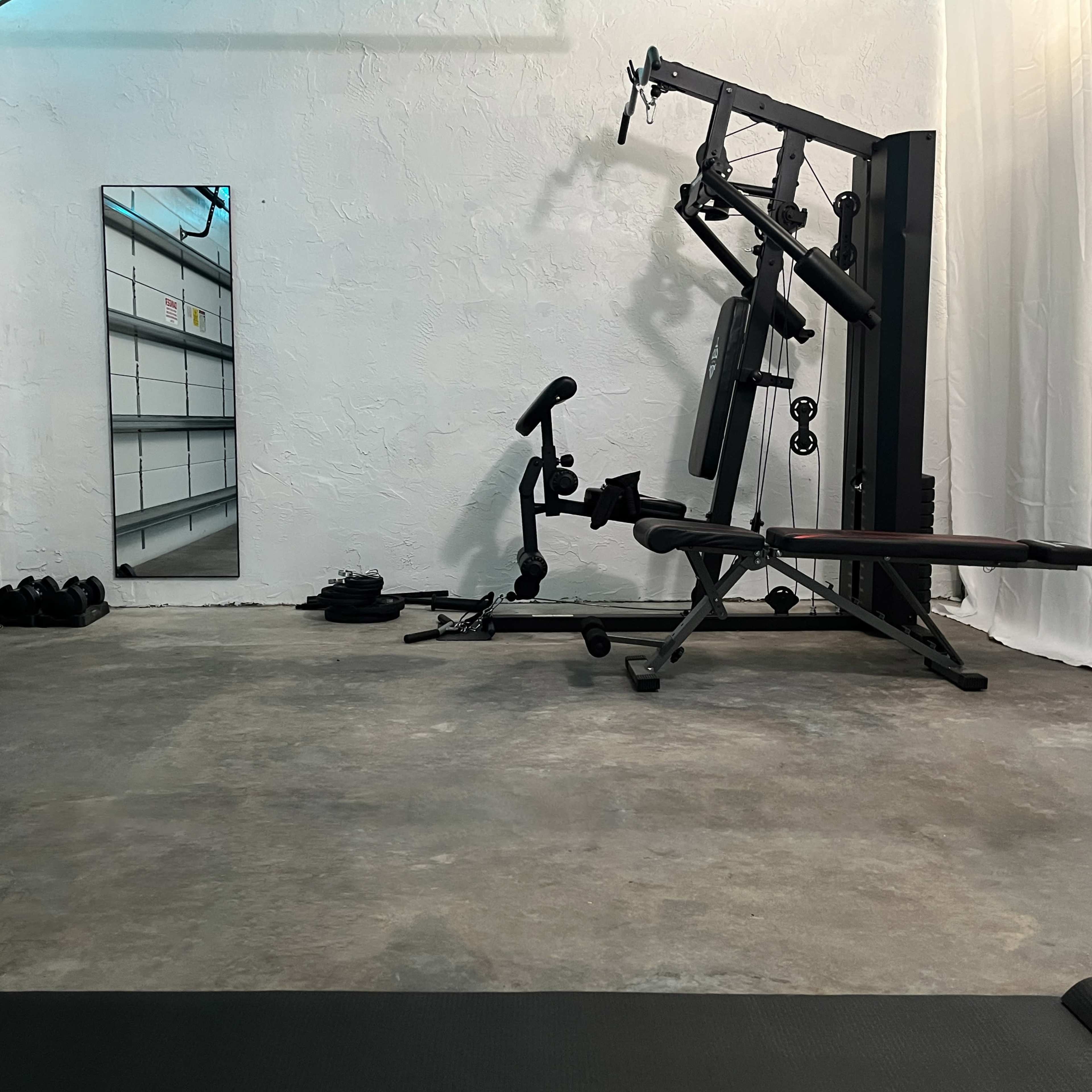 A minimalist home gym setup with fitness equipment, a mirror, and a concrete floor.