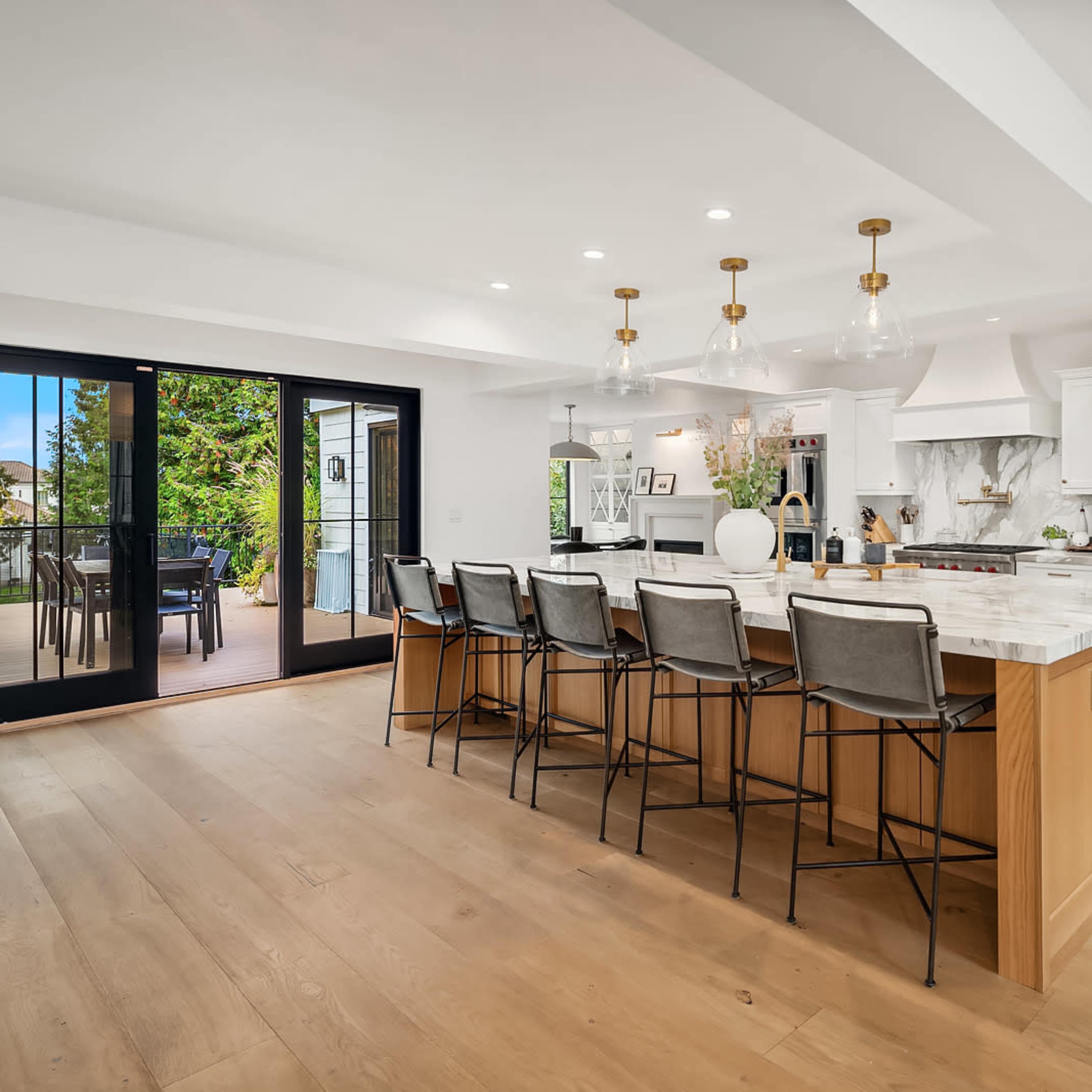 A modern kitchen featuring a large island with seating, white cabinetry, and sliding glass doors leading to an outdoor area.