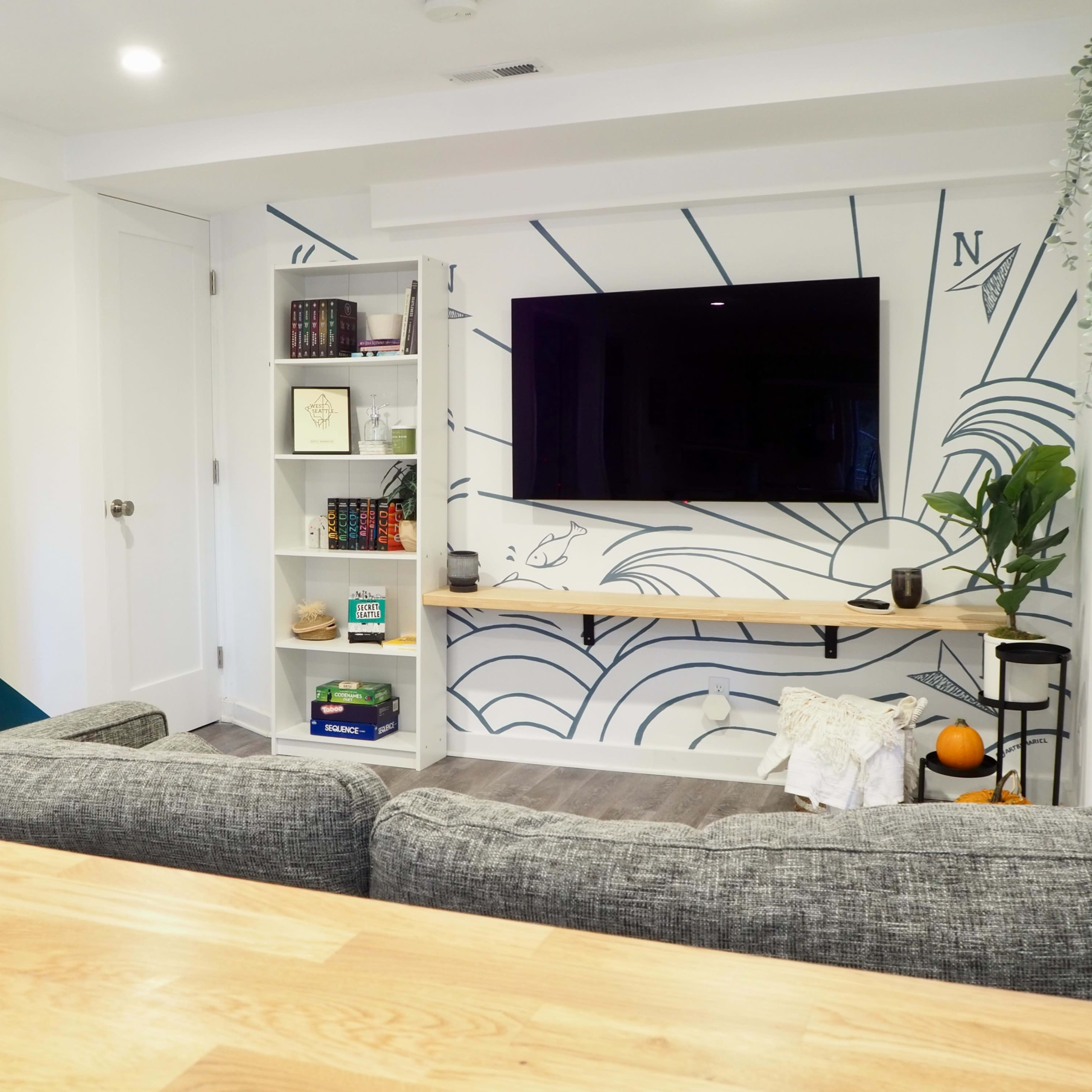 A modern living room with a large wall-mounted television, a bookshelf filled with books, and a decorative wall featuring a sun graphic.