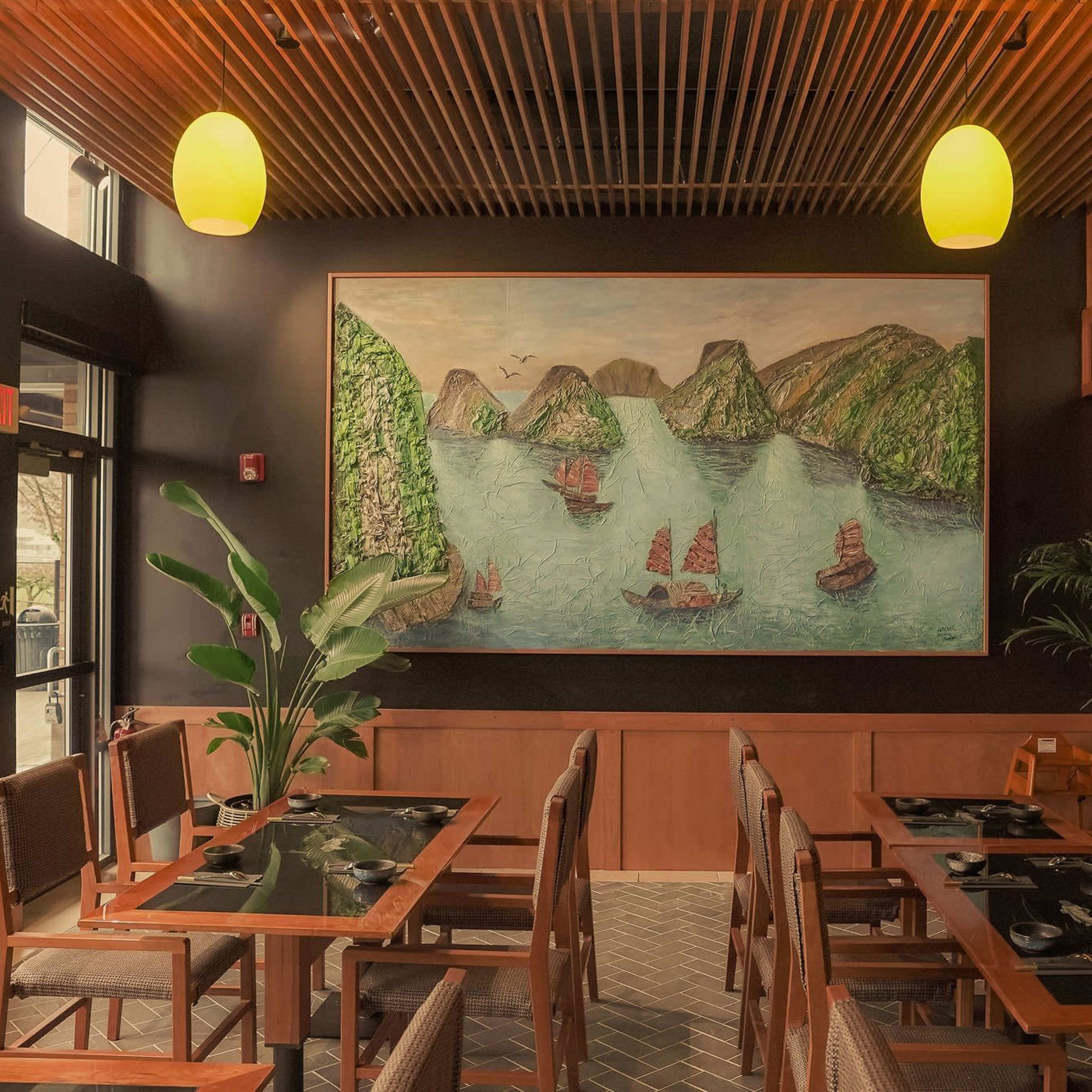 The interior of a restaurant features wooden tables, chairs, and a large mural depicting a coastal scene with boats on water.