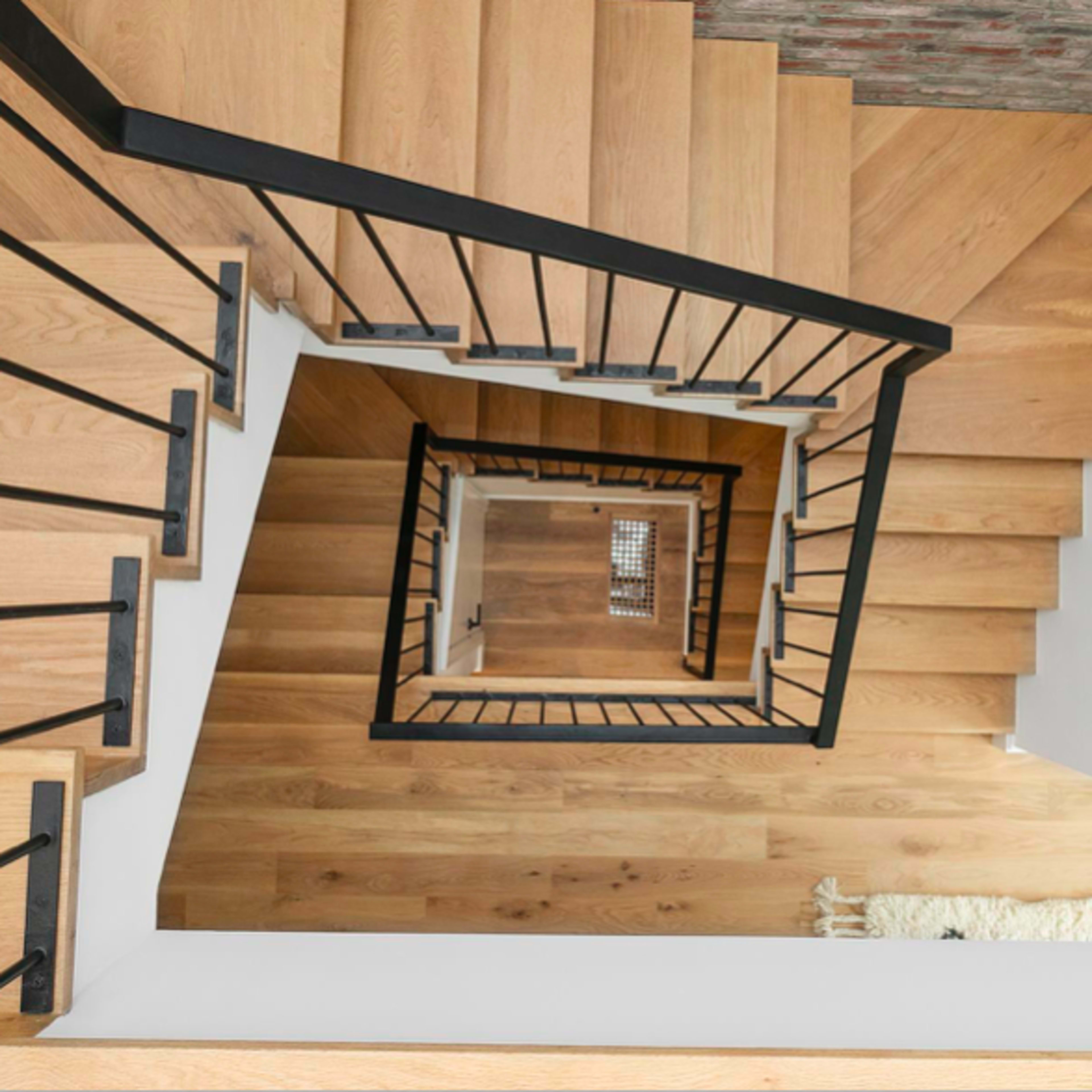 A wooden staircase spirals down with black metal railings, viewed from above.